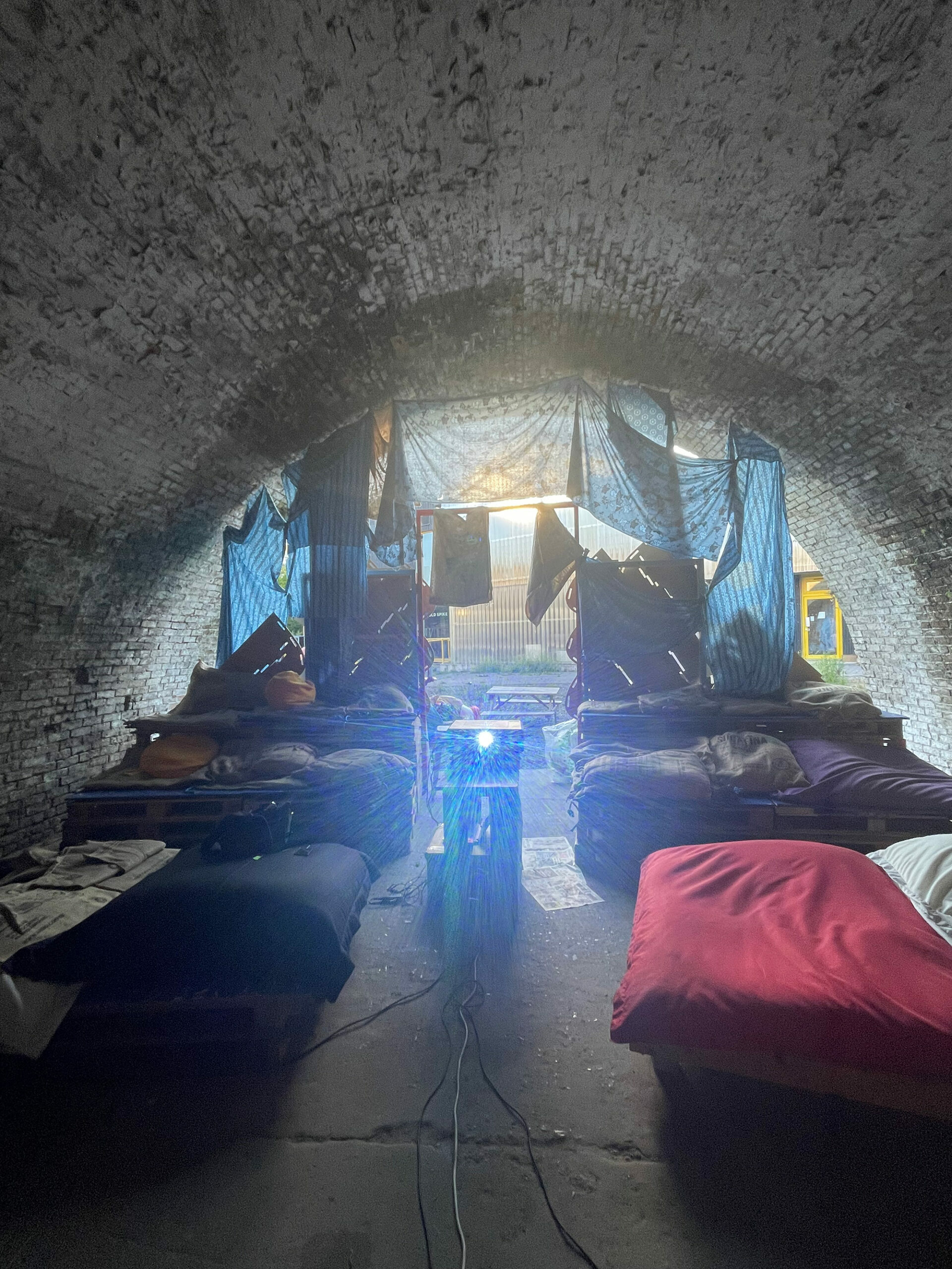 Dimly lit interior of tent in cave, with sleeping bags and cushions arranged inside.