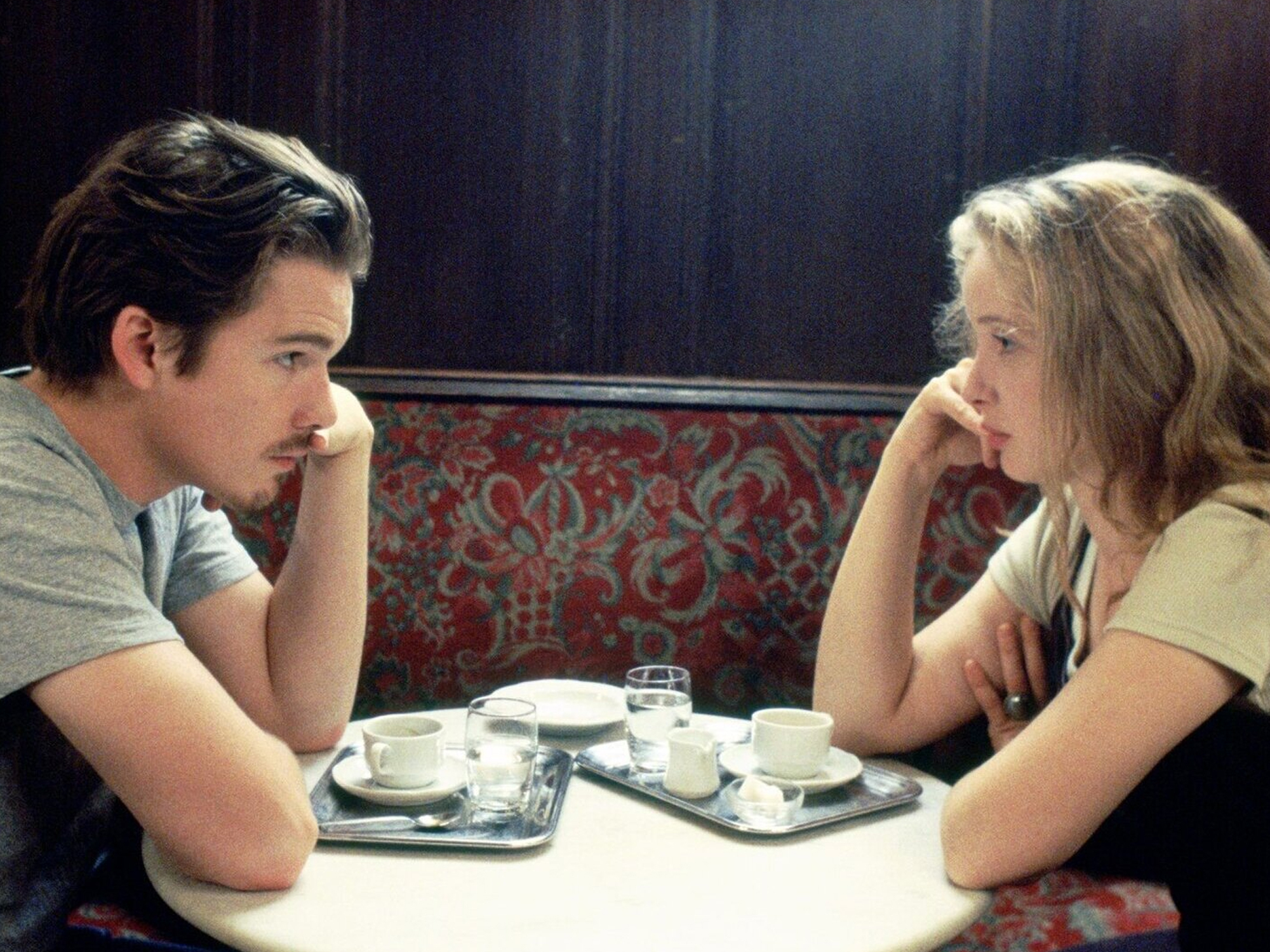 Ethan Hawke and Julie Delpy in Before Sunrise sitting at a table looking at each other.