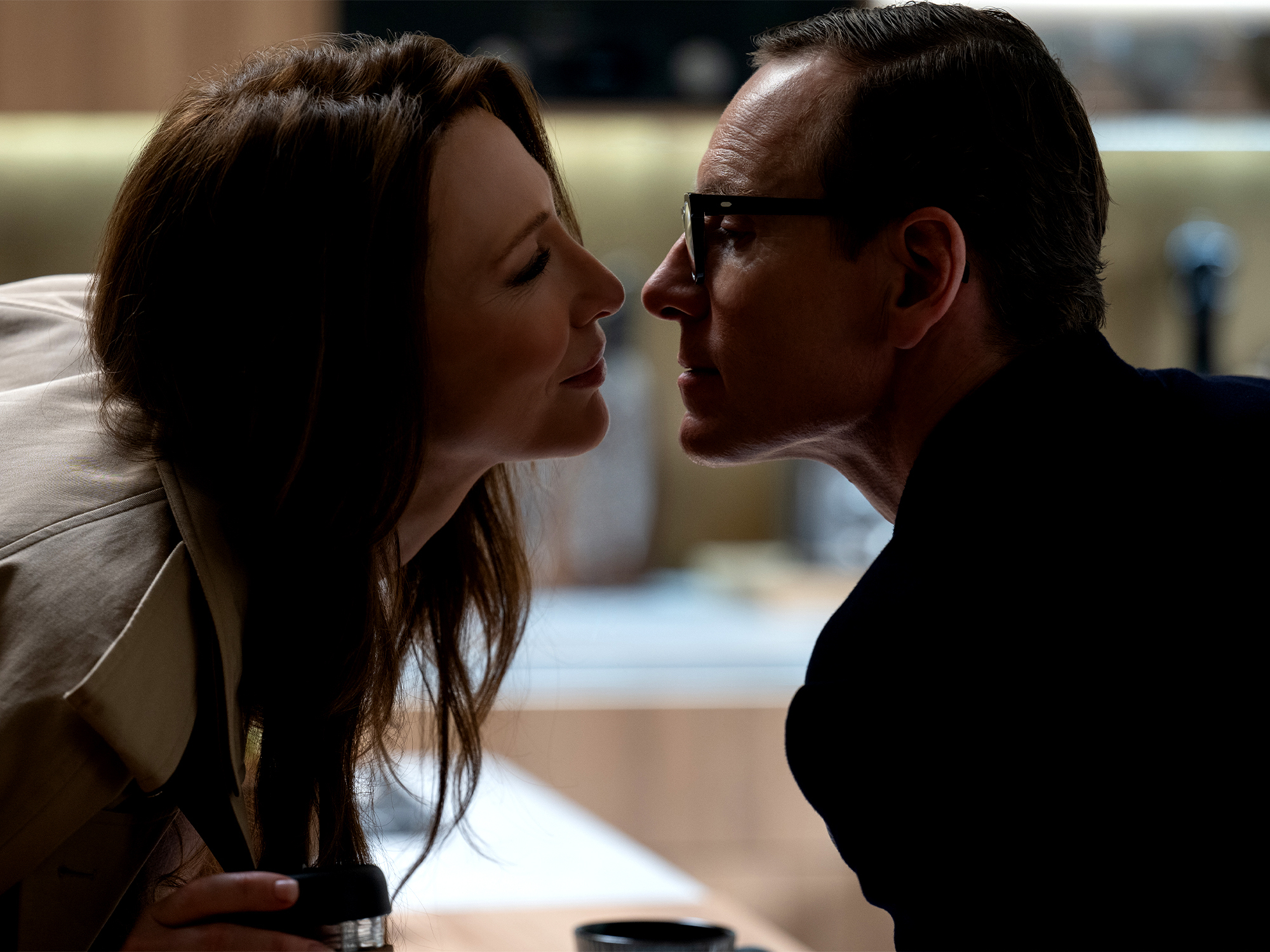 Man and woman with dark hair facing each other closely in intimate pose, soft lighting, blurred background.