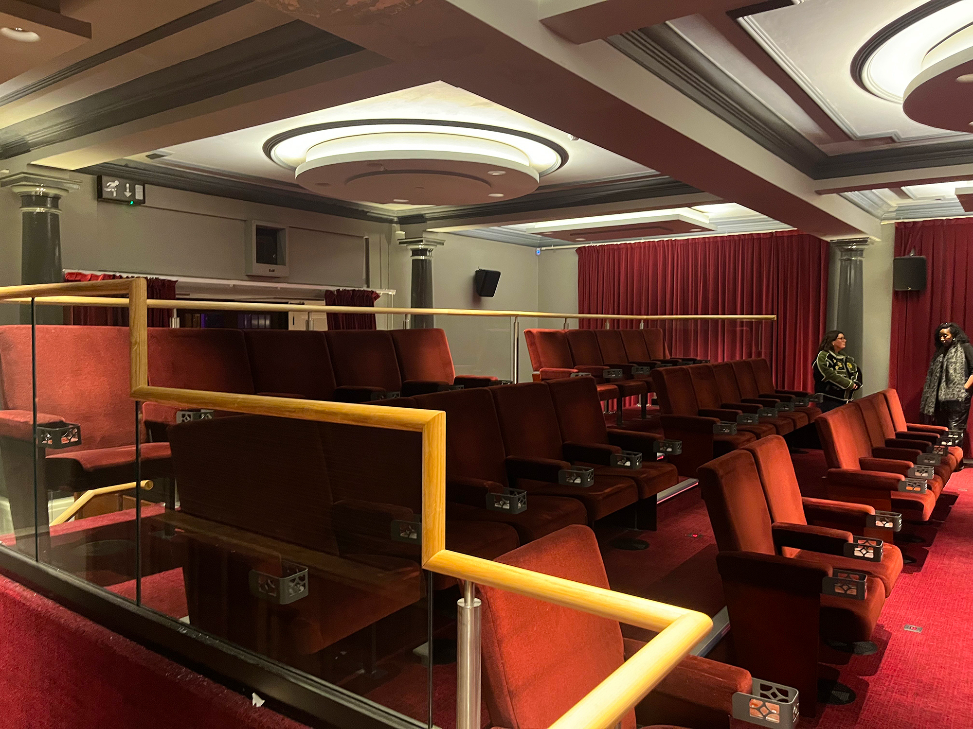 Red velvet seats in an elegant theatre with ornate ceiling and stage curtains.