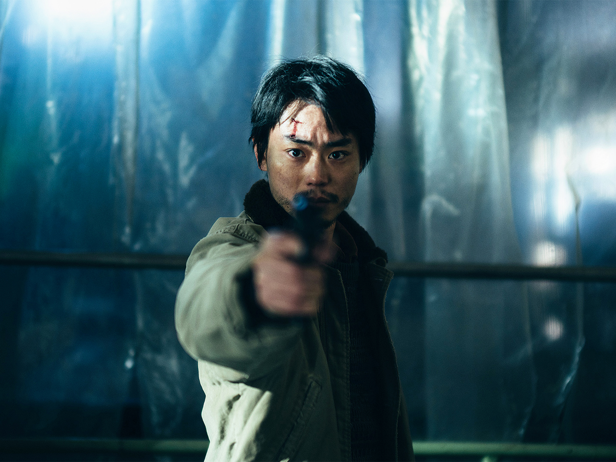 A man with dark hair pointing a gun in a dimly lit, rainy setting.