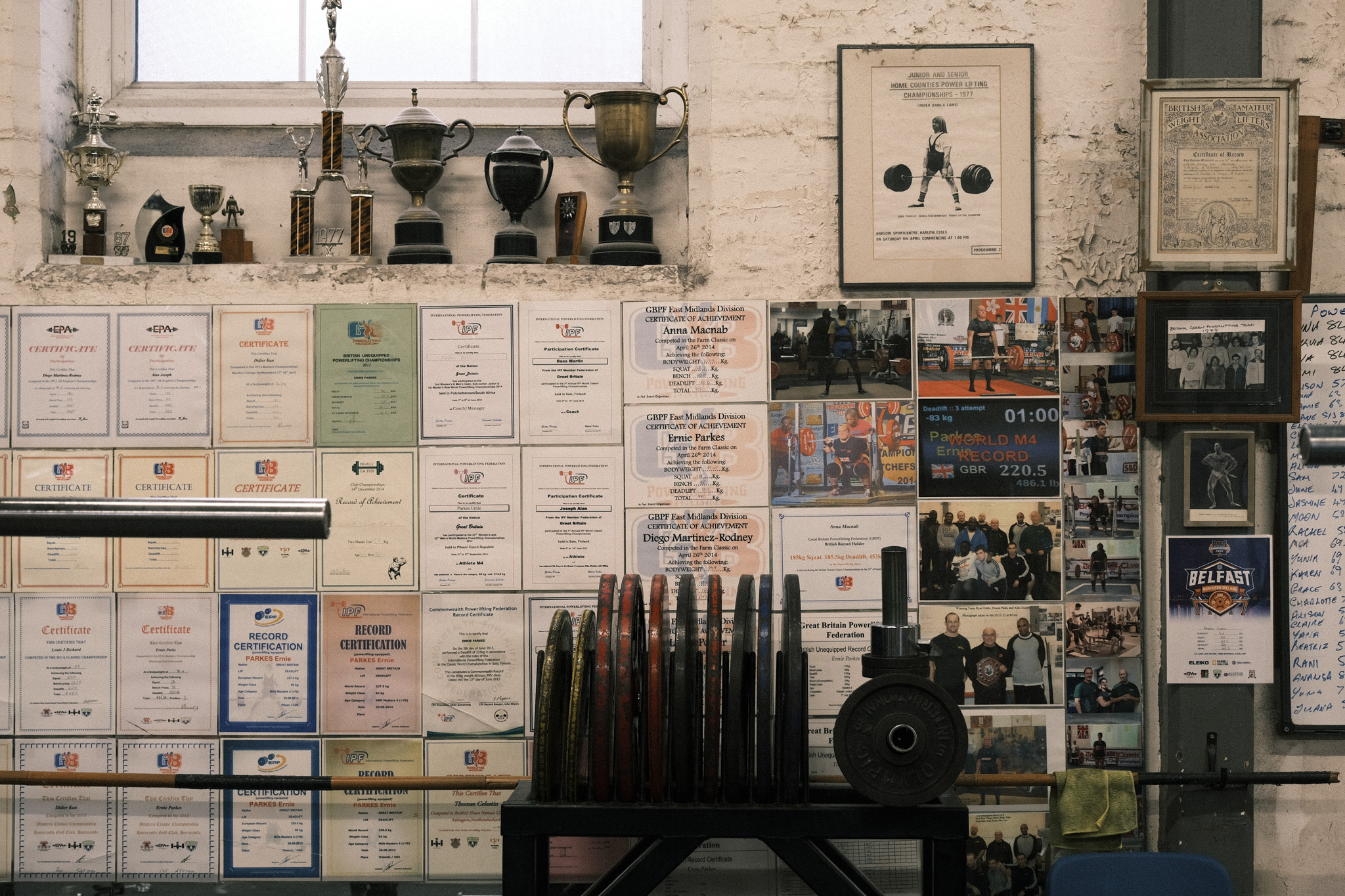 Vintage laboratory with cream cabinets, brass instruments, certificates covering walls, ammunition samples, and scientific equipment on shelves.