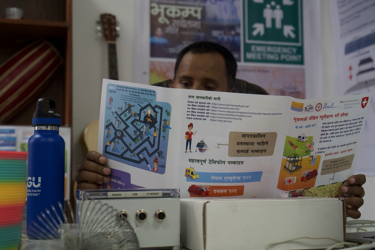 Man holds open colourful educational booklet with maze and illustrations. Office setting with posters on wall behind him.