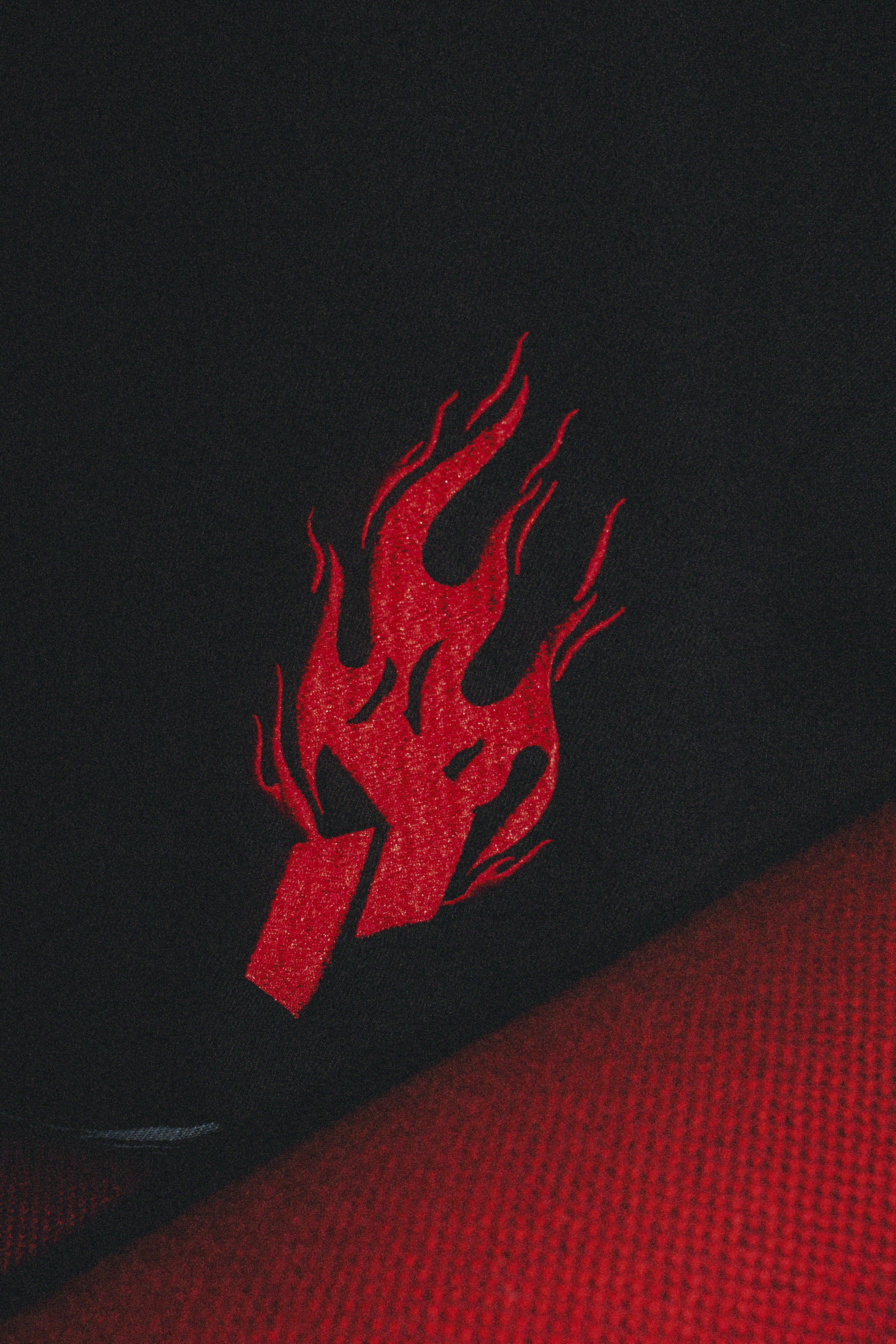 Red flame-like logo on black fabric surface with red textured material visible in bottom right corner.