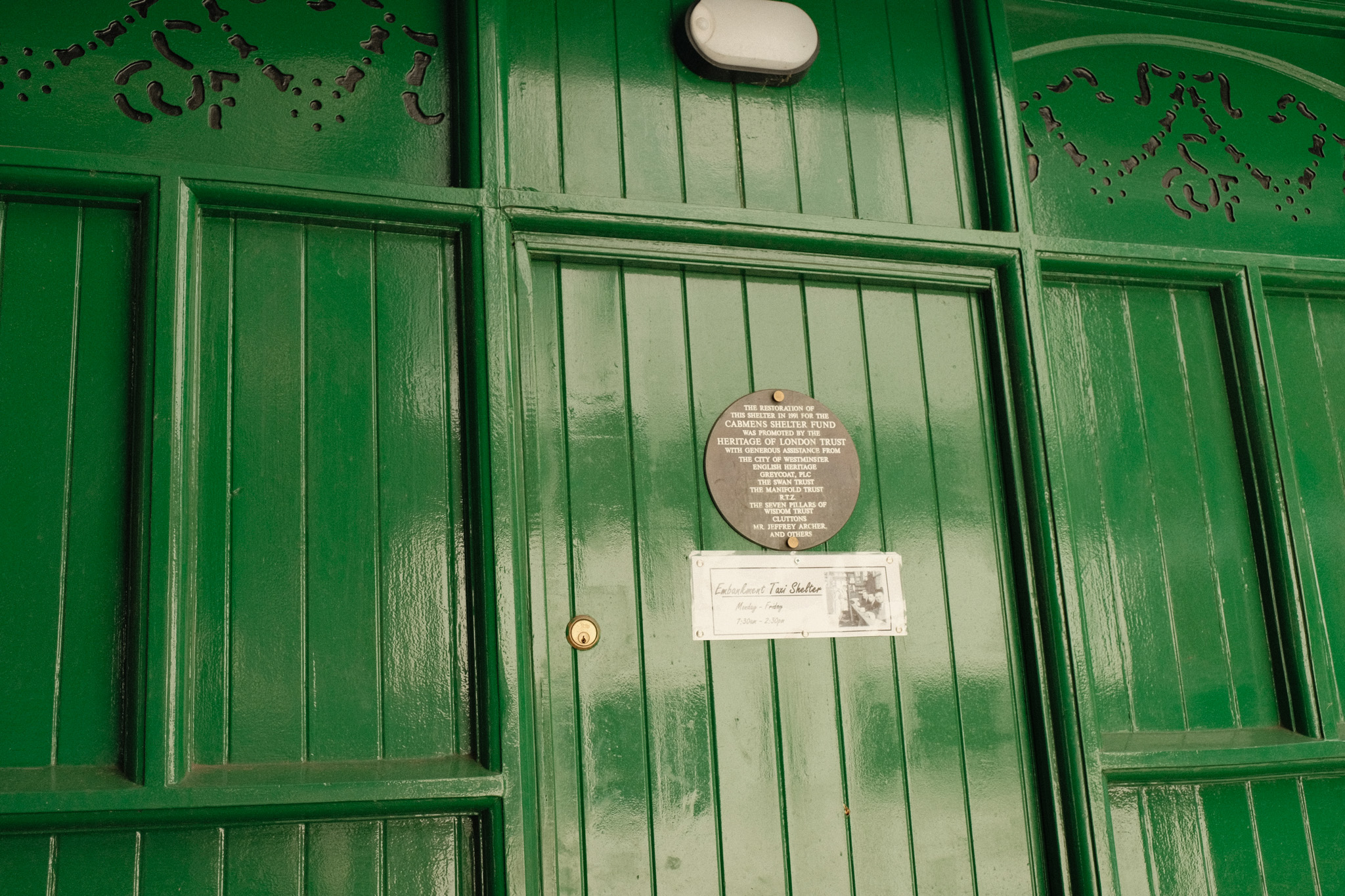 Green wooden Victorian shopfront with vertical planked door, decorative moulding, and circular commemorative plaque mounted centrally.