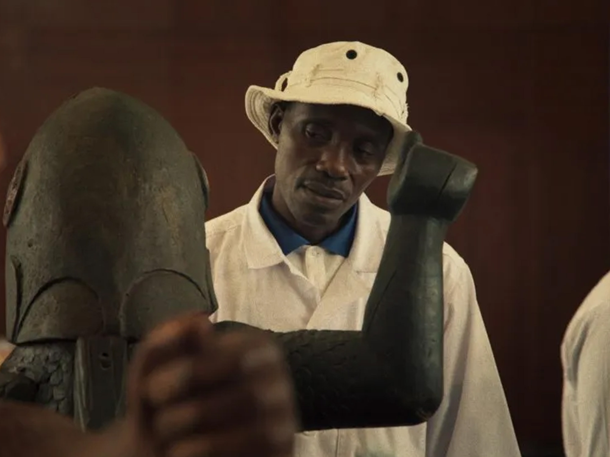 A man wearing a safari hat and shirt, holding a shovel.