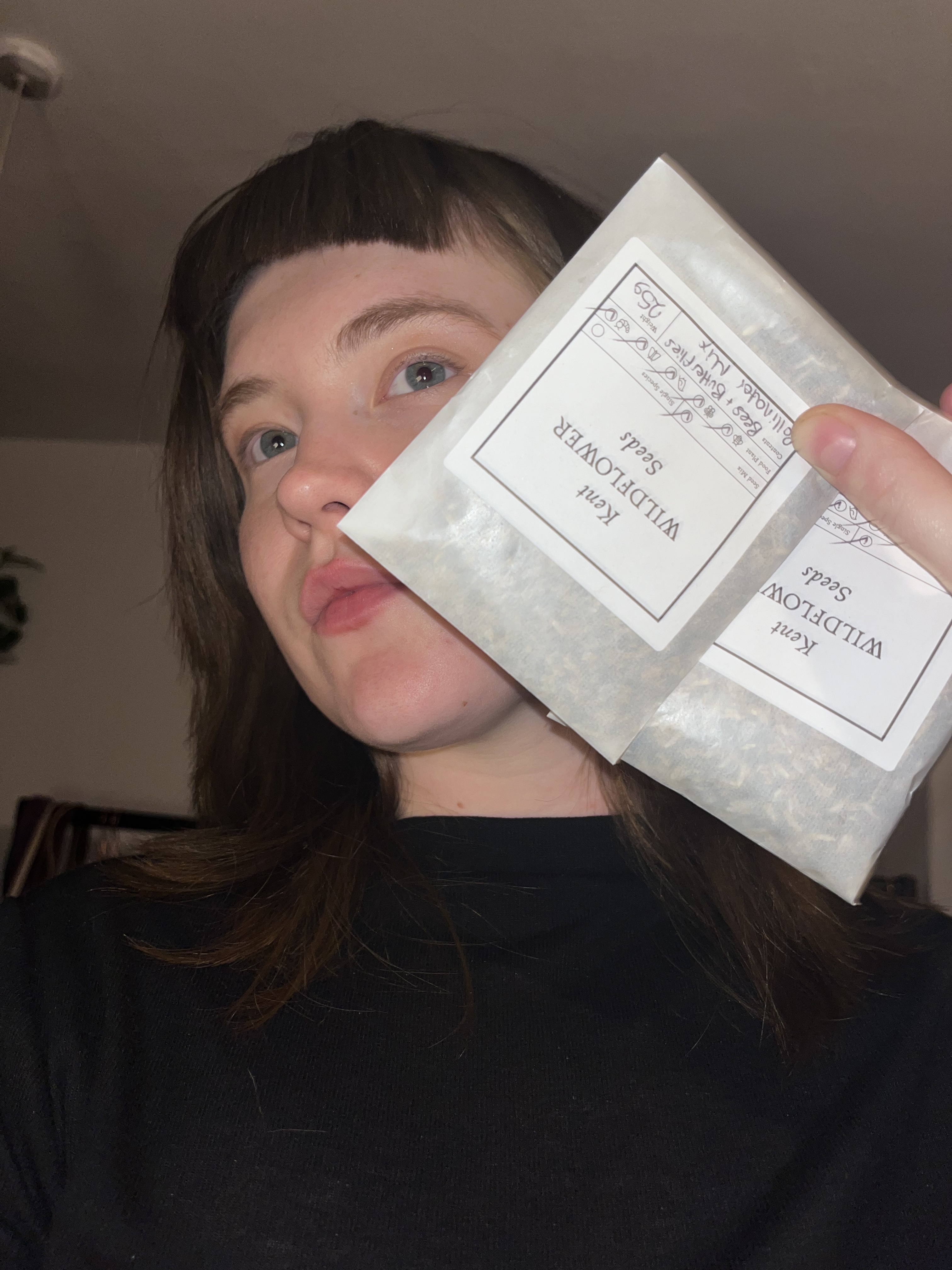 Woman with brown hair and pink face mask holding white skincare product packets labelled "SKINCEUTICALS" in black text.