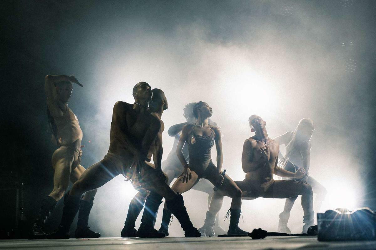 Silhouettes of people sitting on bench against bright white backdrop with dramatic lighting and smoke effects on stage.