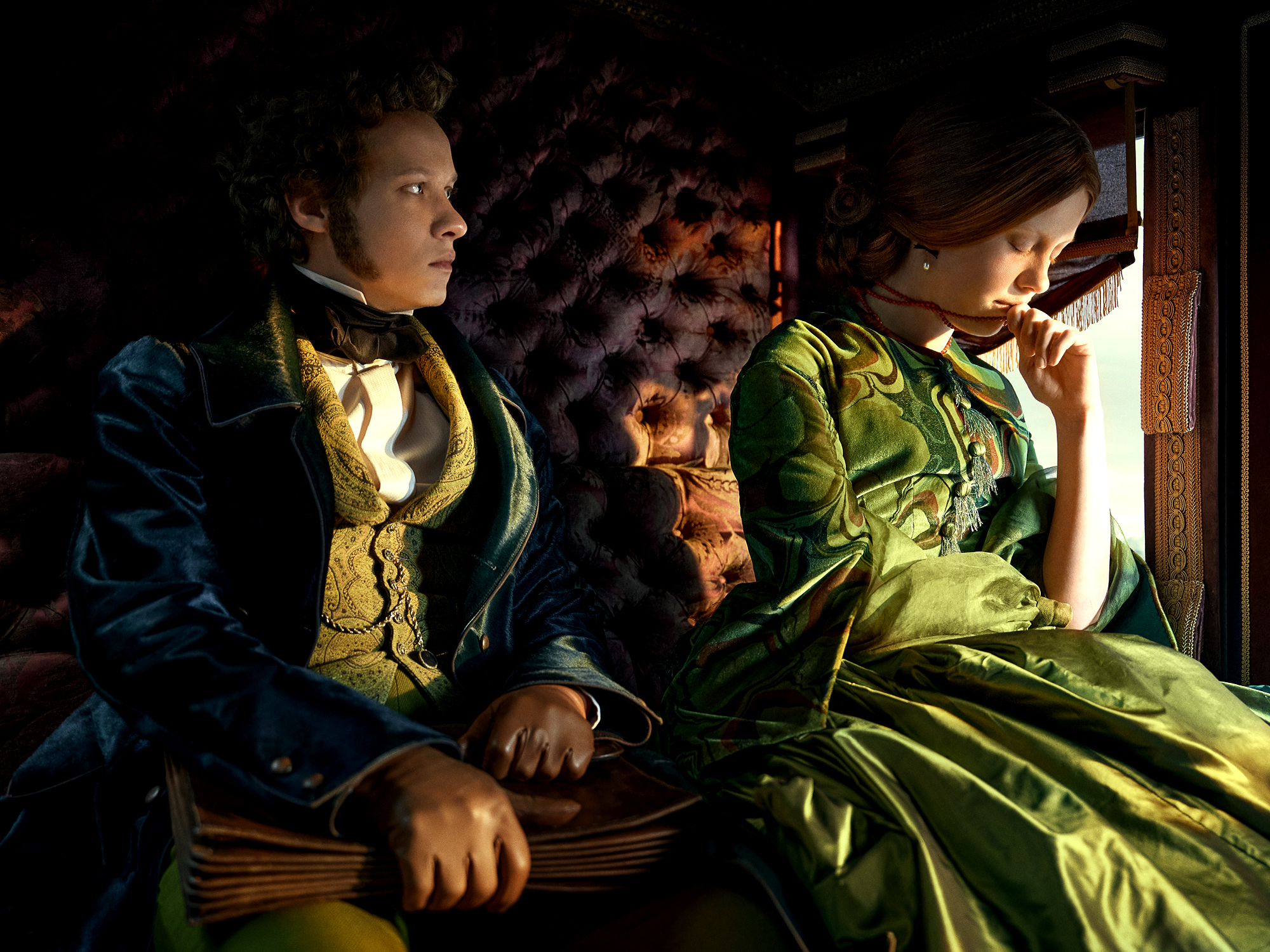 Man and woman in period dress sit cart - man in blue with yellow waistcoat, woman in green dress by window light. Dark interior.
