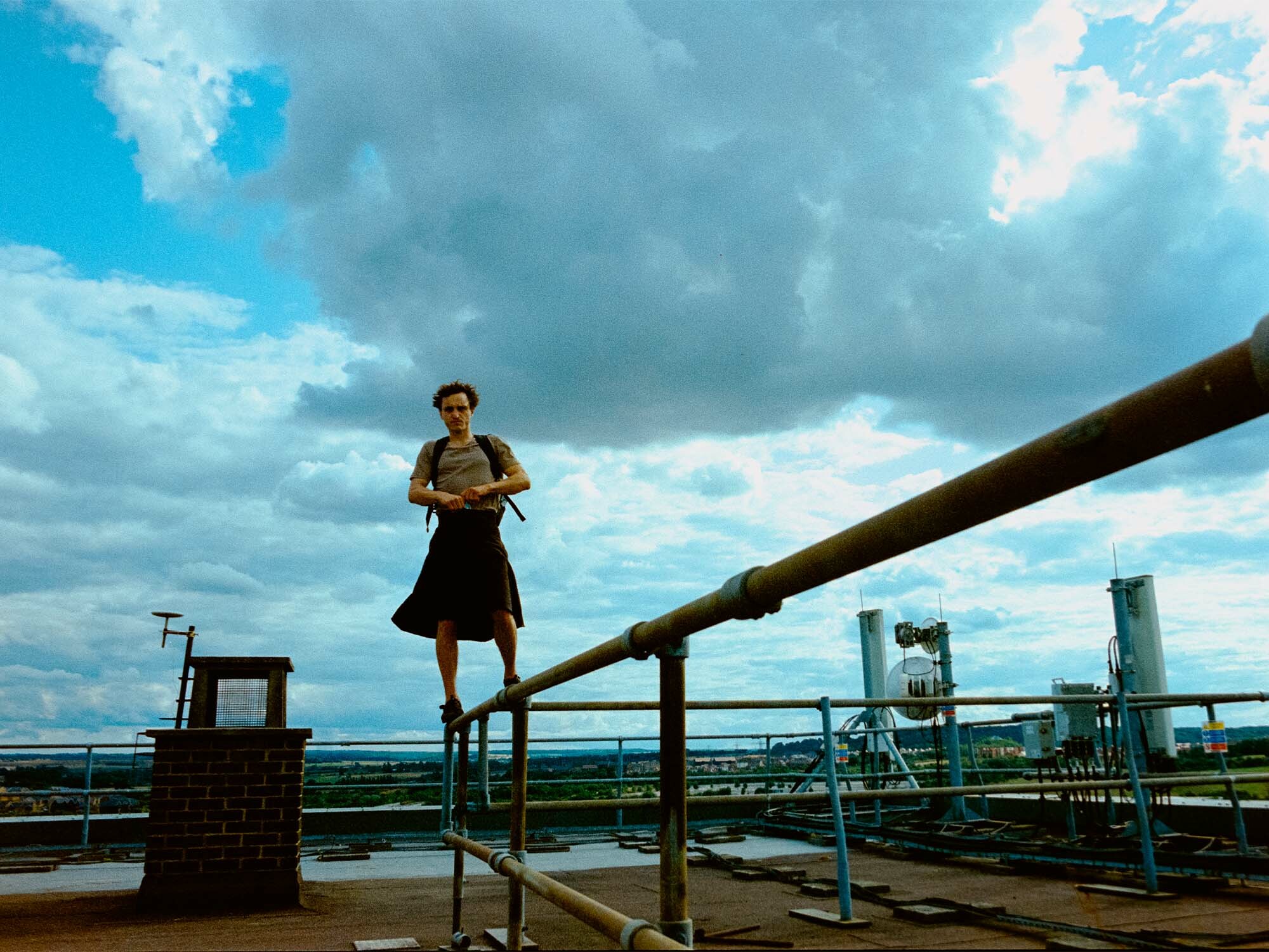 A person standing on a railing overlooking an industrial landscape, with cloudy sky in the background.