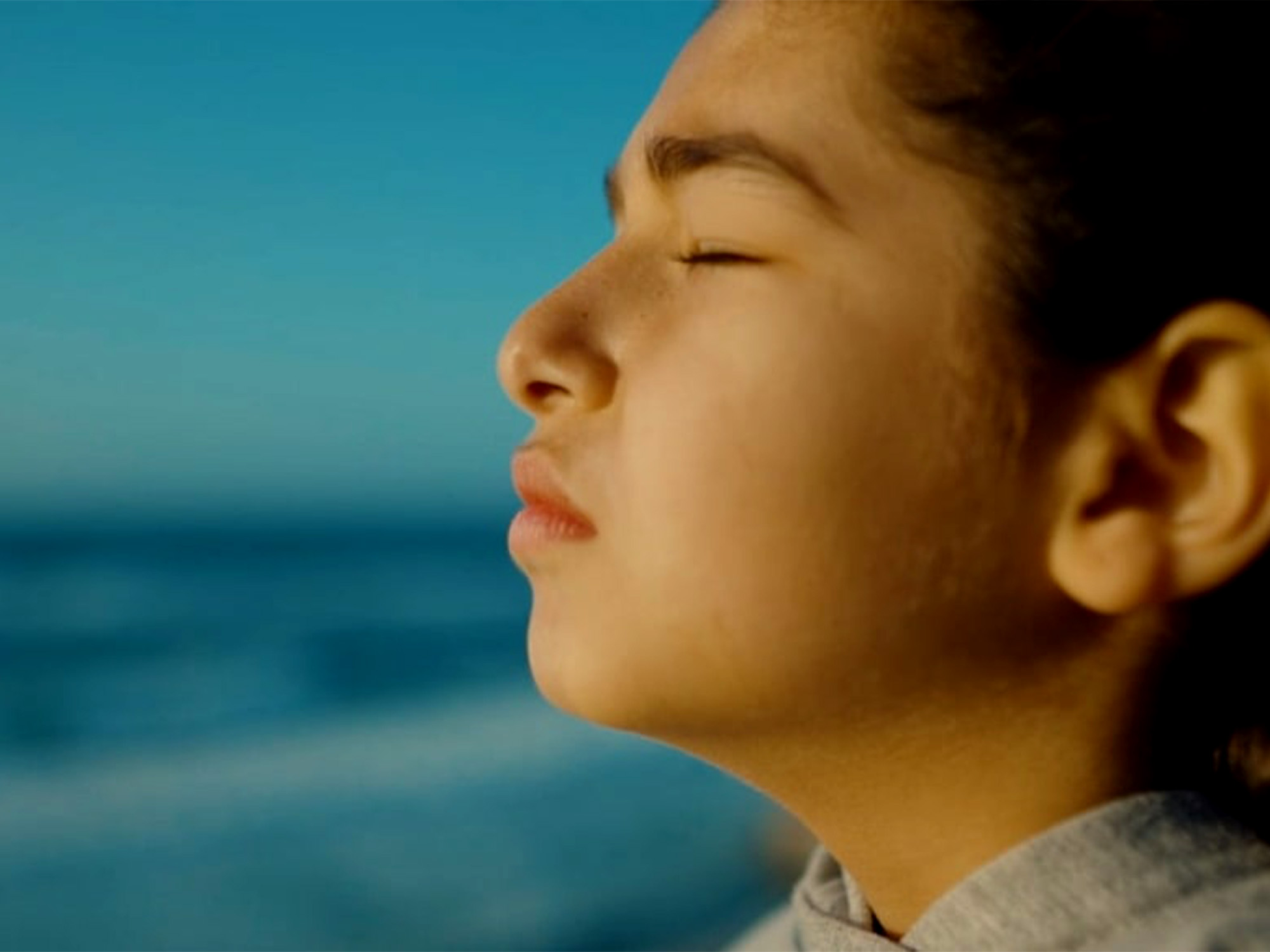 Person in profile with closed eyes against blurred blue background, warm golden lighting on face.