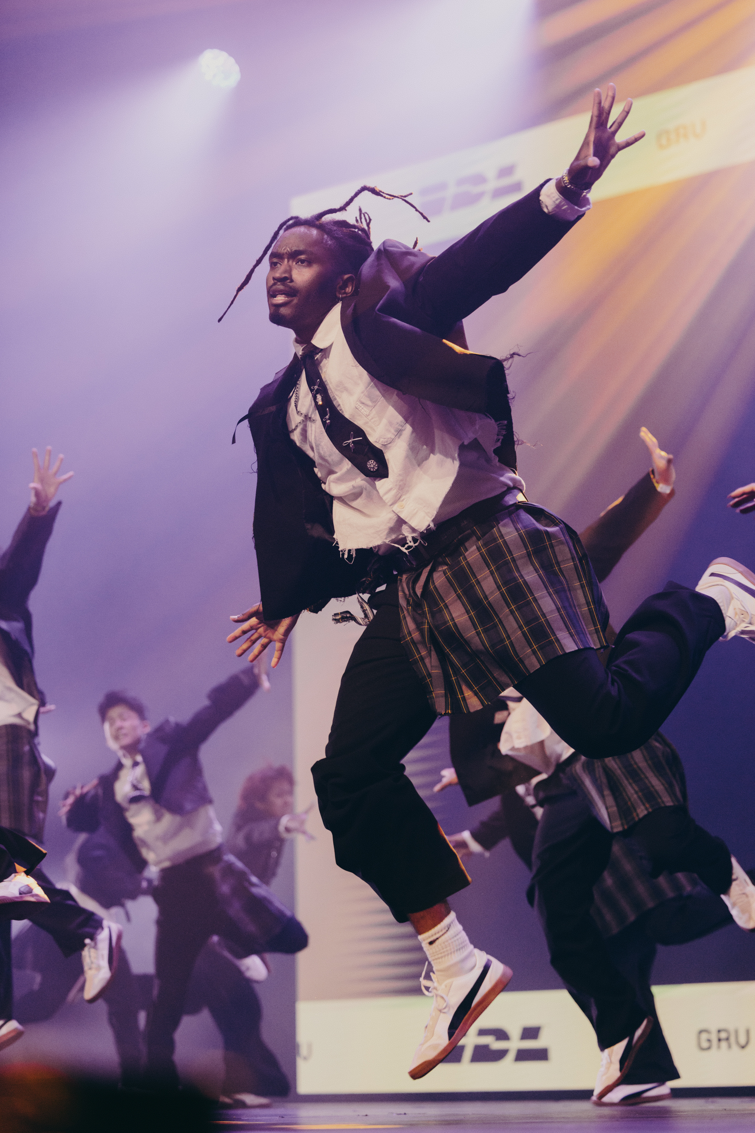 Digital illustration showing figure in dark jacket and tartan kilt jumping with arms raised against purple sky with golden light rays.