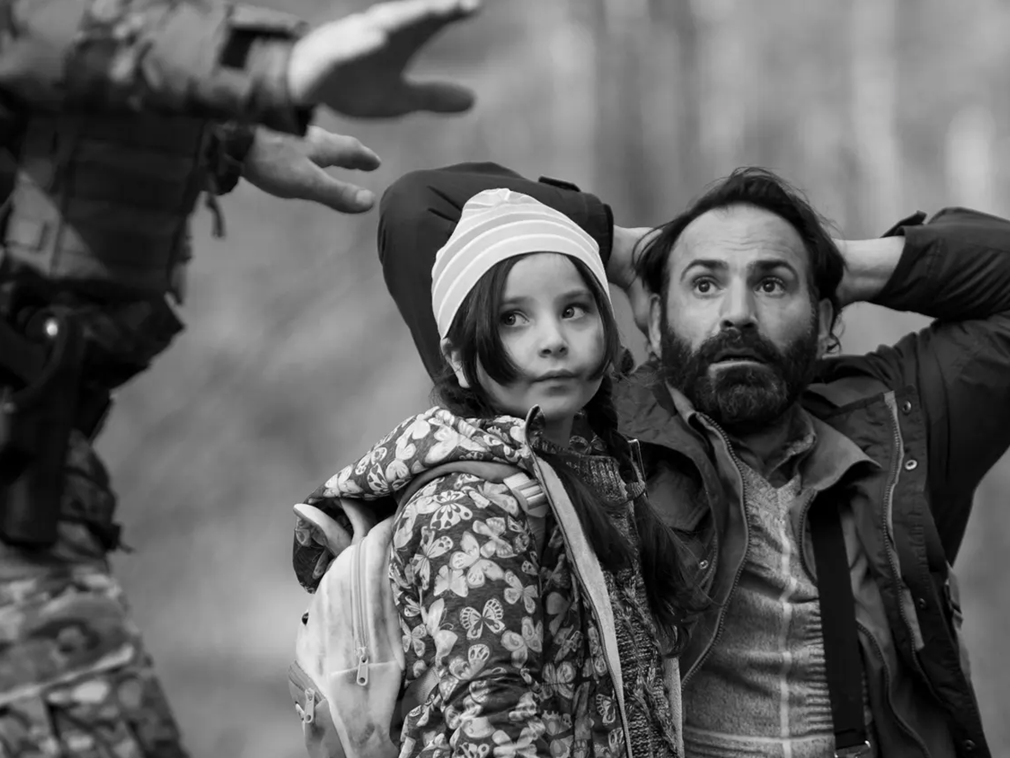 A man with a beard embracing a young girl wearing a floral coat and hat. The image is in black and white.