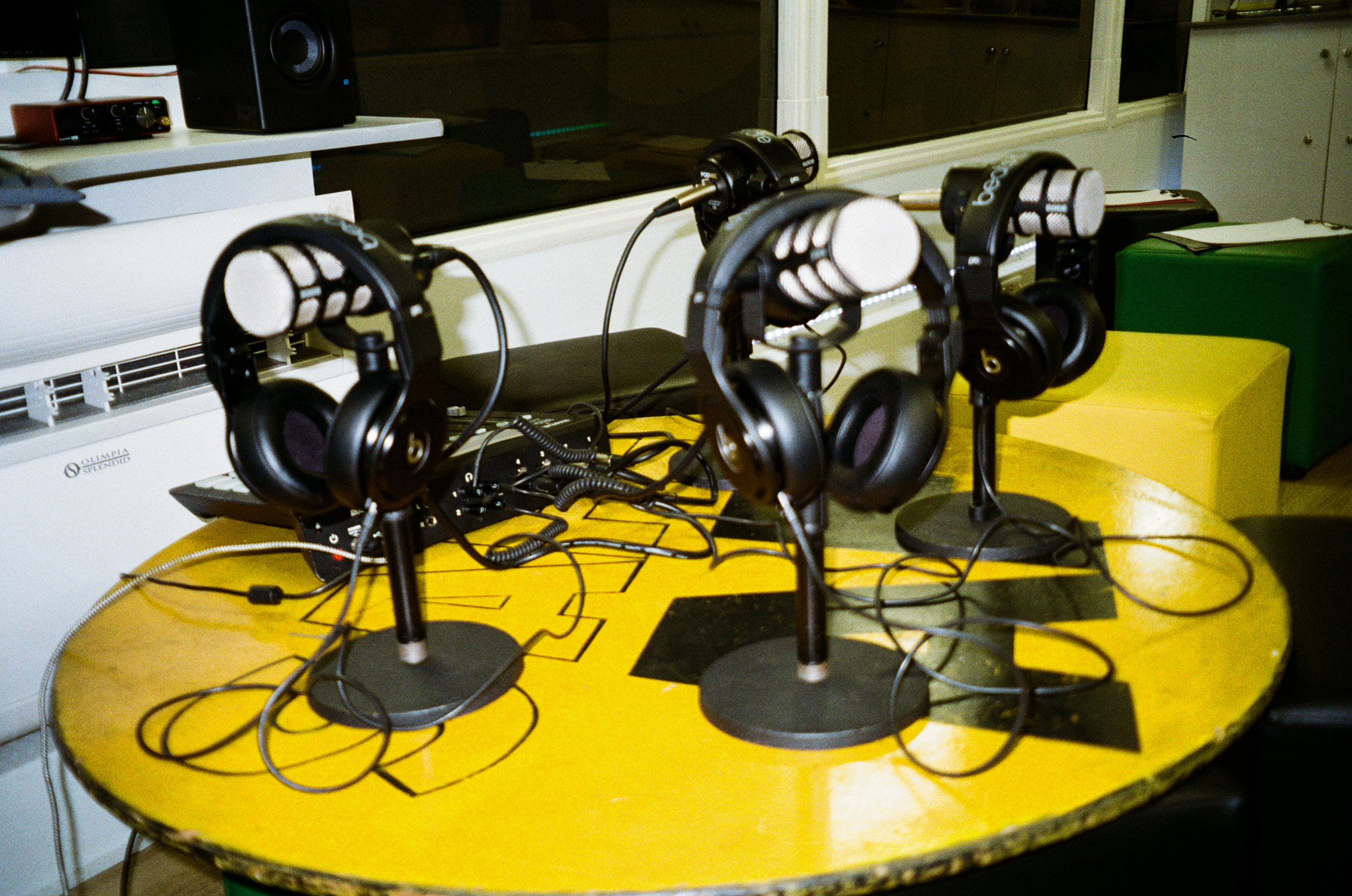 Yellow round table with four black microphone stands and headphones, cables scattered across surface, recording studio setup.