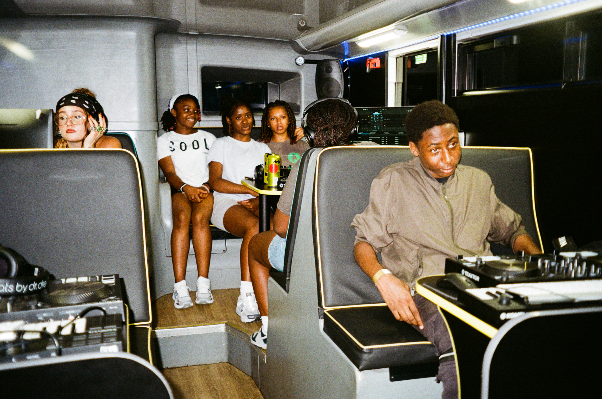 People seated in grey aircraft cabin seats, man in foreground wearing beige shirt, group of passengers visible in background rows.