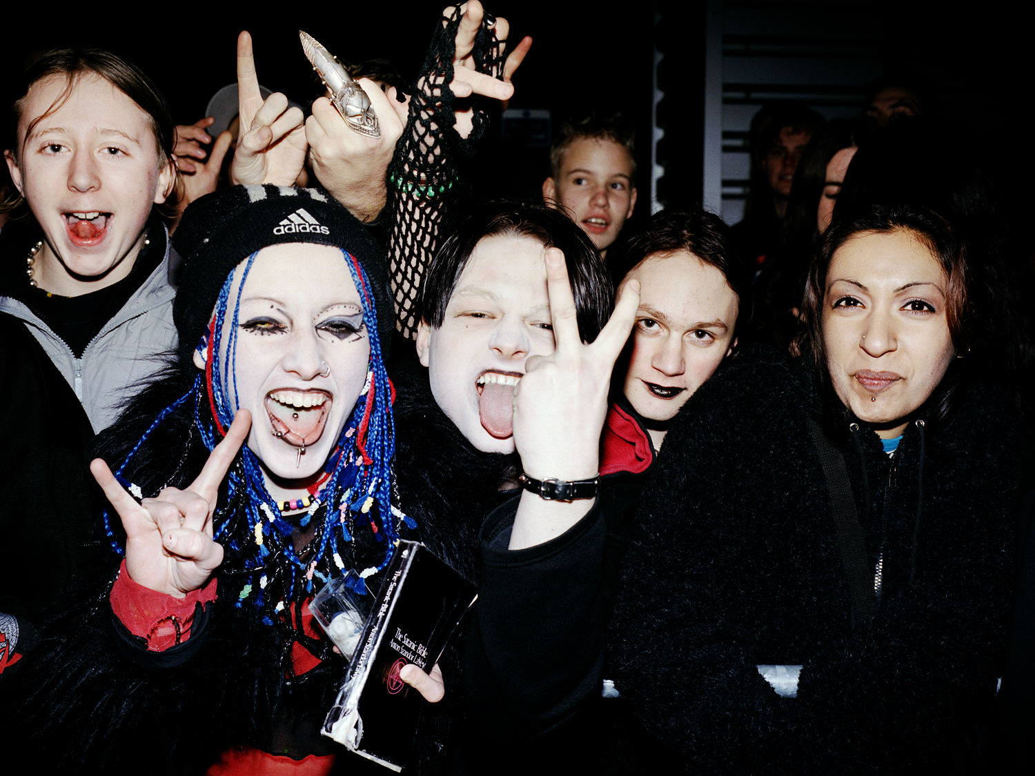 Group of people in gothic/alternative clothing making rock gestures and silly faces. Blue and black hair, dark makeup, tongues out.