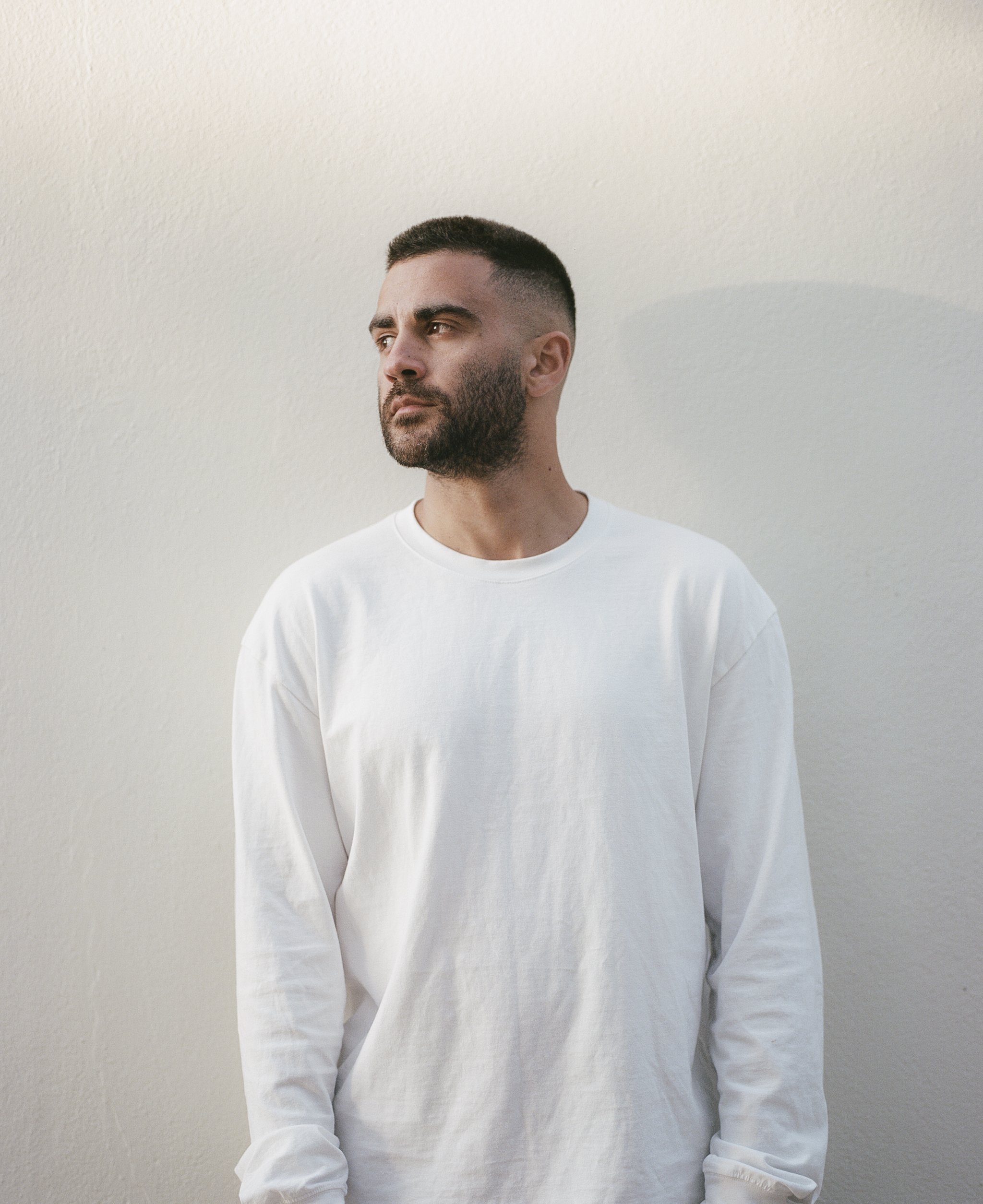 A man with a beard wearing a white long-sleeved shirt.