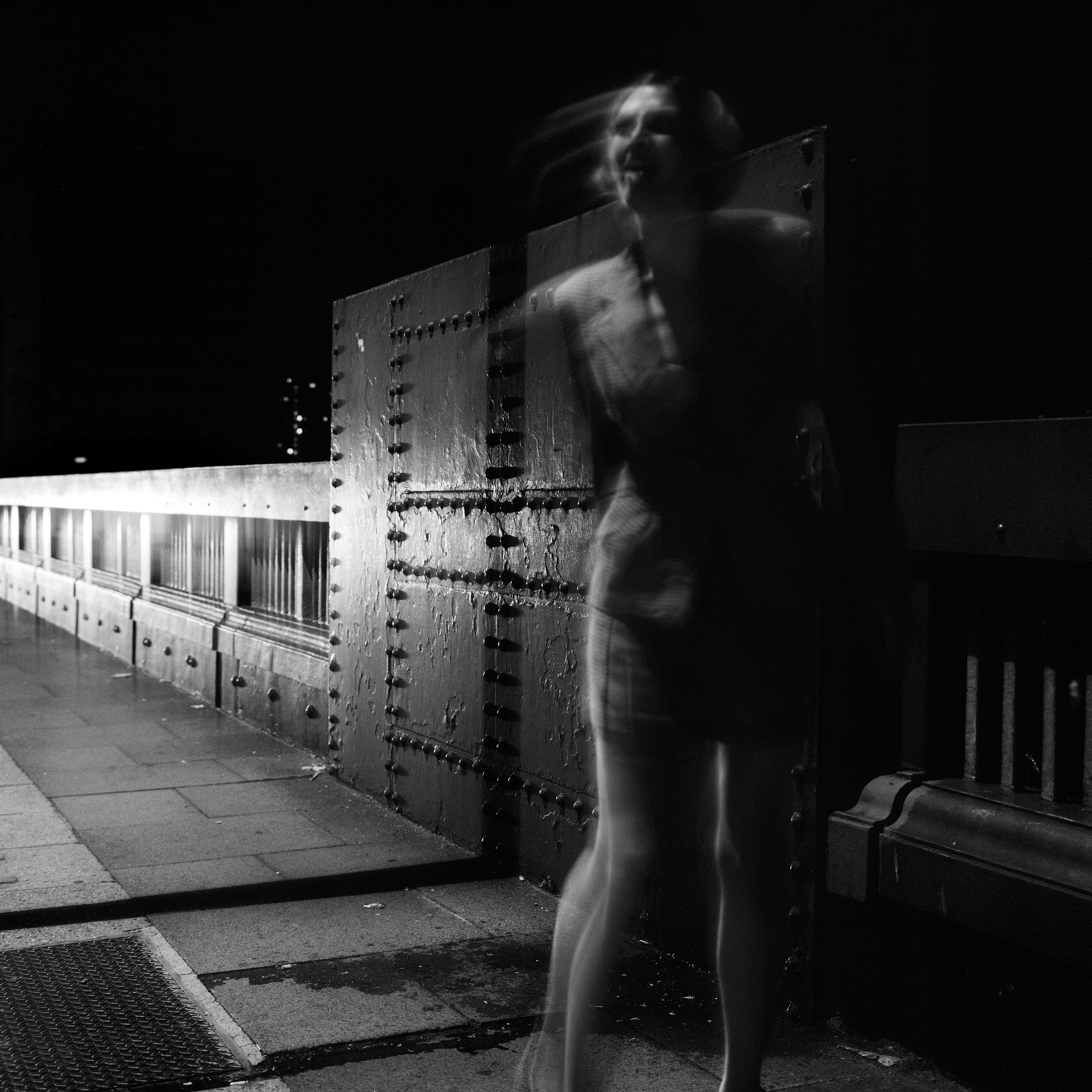 Blurred figure stands before large industrial control panel with switches and gauges in black and white image.