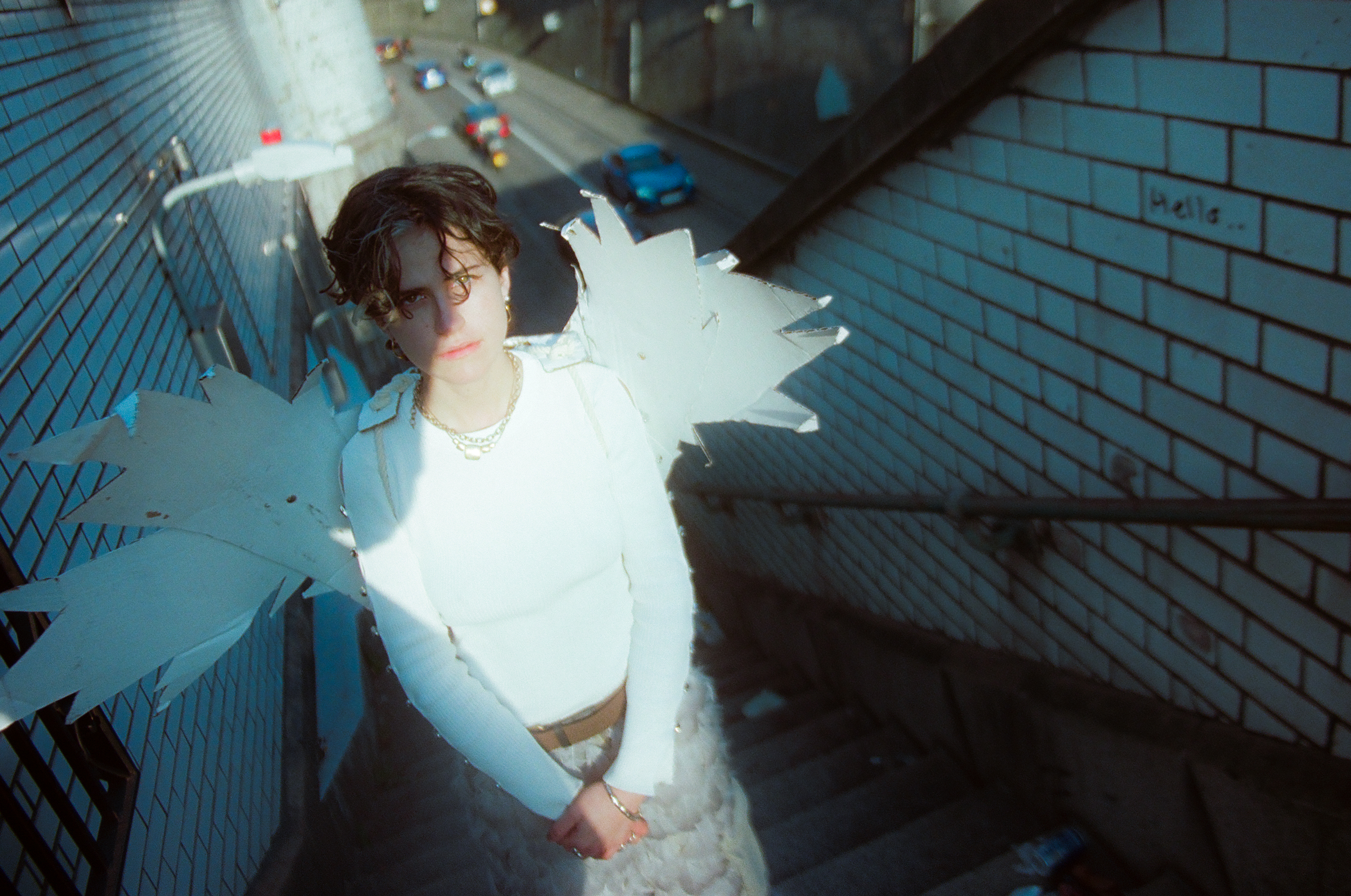Person in white dress floating underwater in blue-tiled swimming pool, arms outstretched, fabric billowing around body.