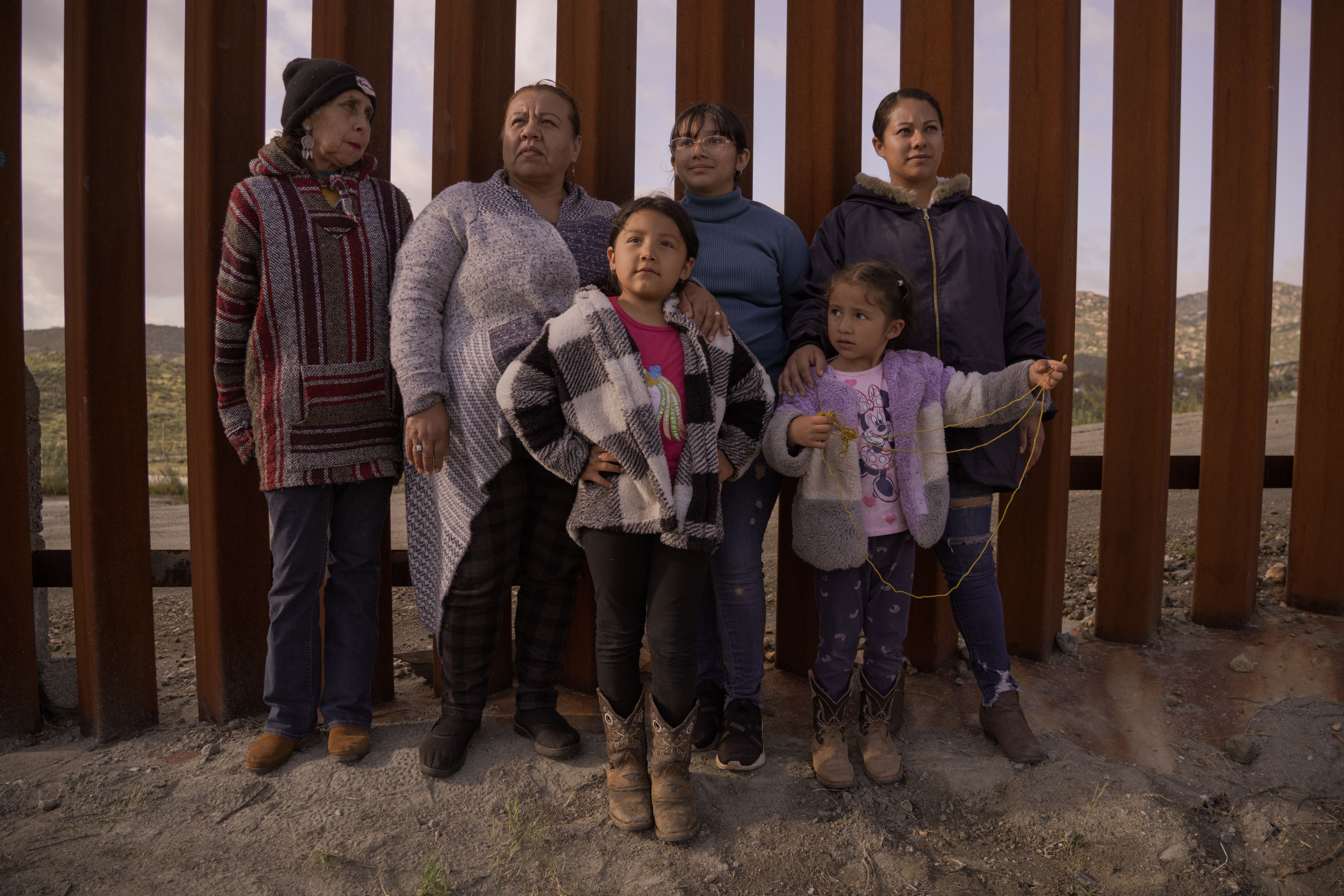 Family of 6 people, including 3 children, standing together in front of a wooden fence.