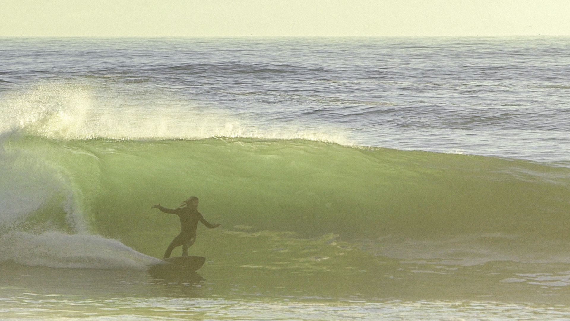 Wave crashing over surfer riding a green surfboard on a calm ocean.