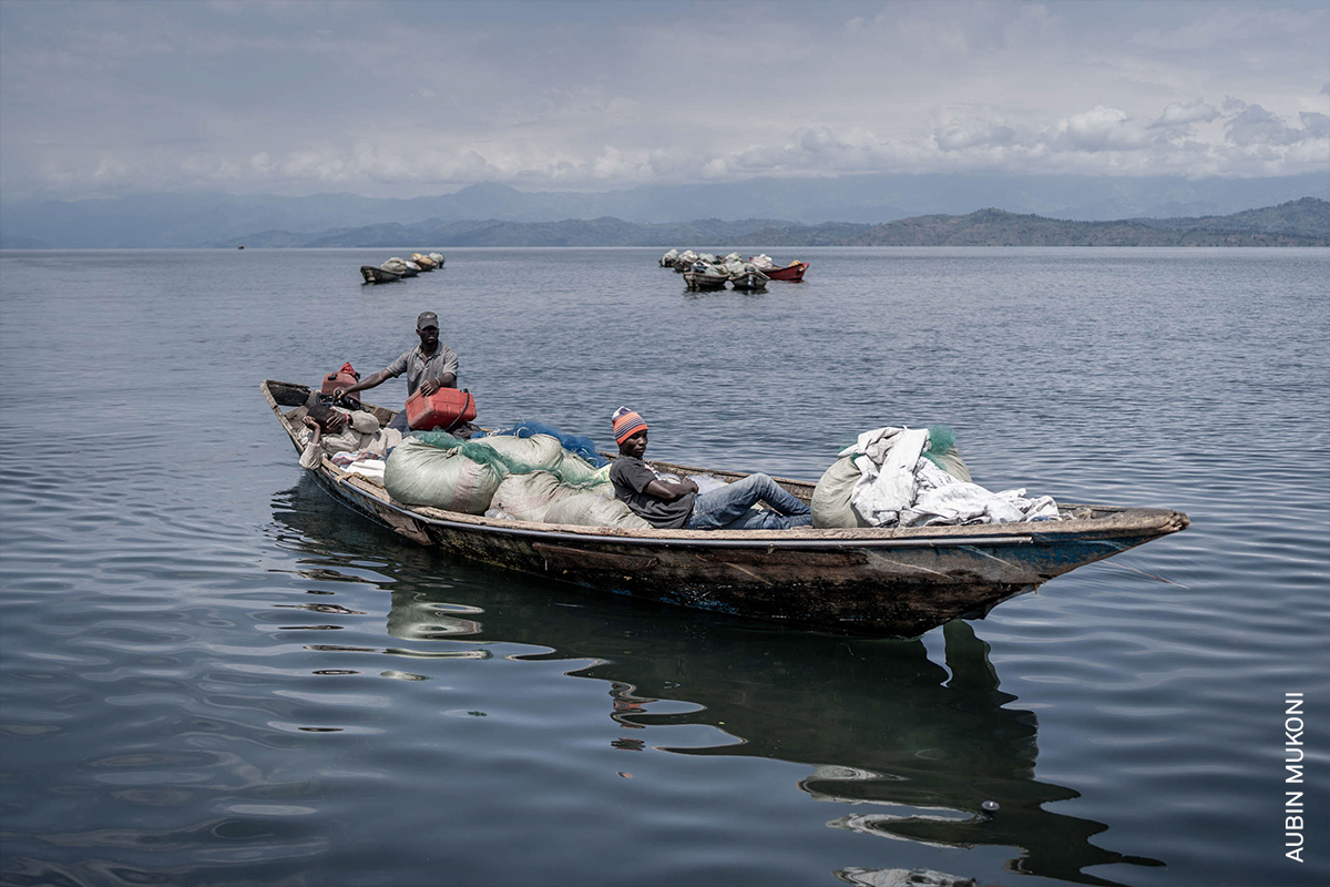 Fishing boats on calm waters surrounded by mountains, with people aboard the boats.
