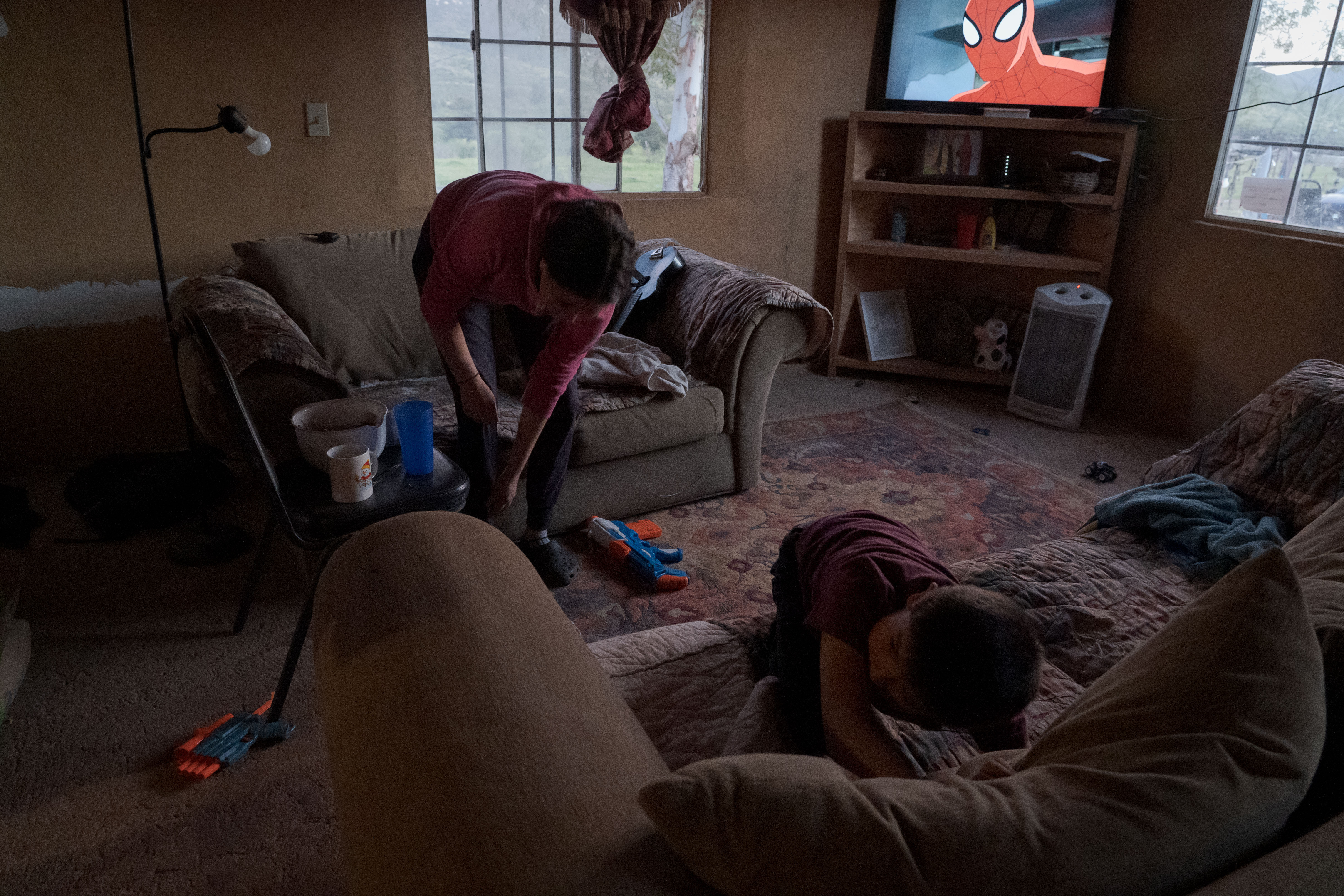 Cluttered room with cushions, a television, and a person sitting on the floor.