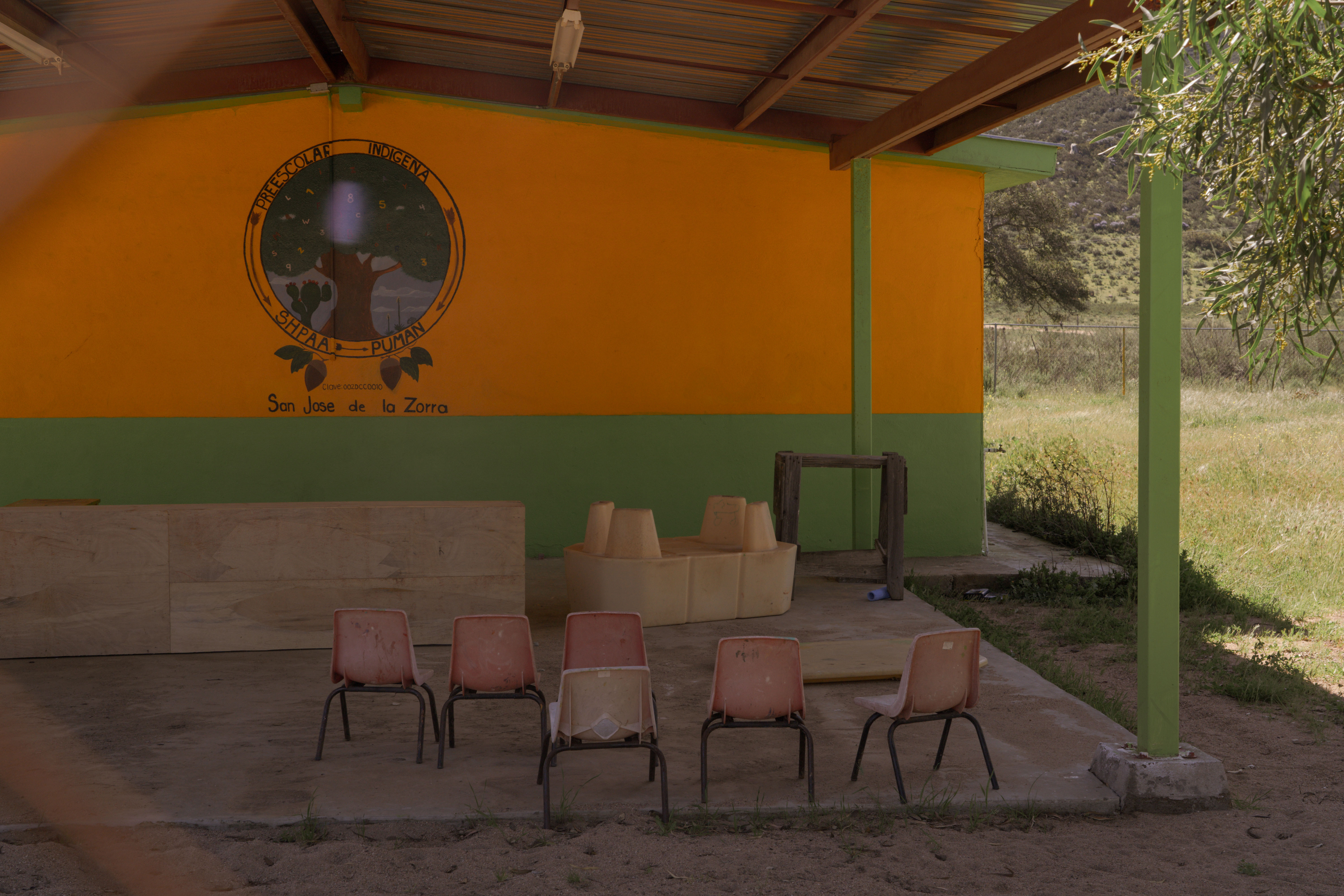 Outdoor seating area with orange and green walls, wooden benches, and a decorative round wall hanging.