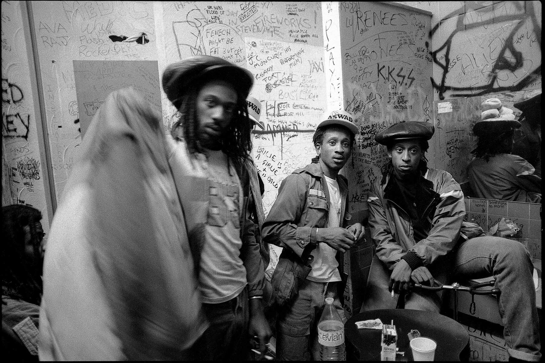 Group of young men with graffiti-covered wall behind them.
