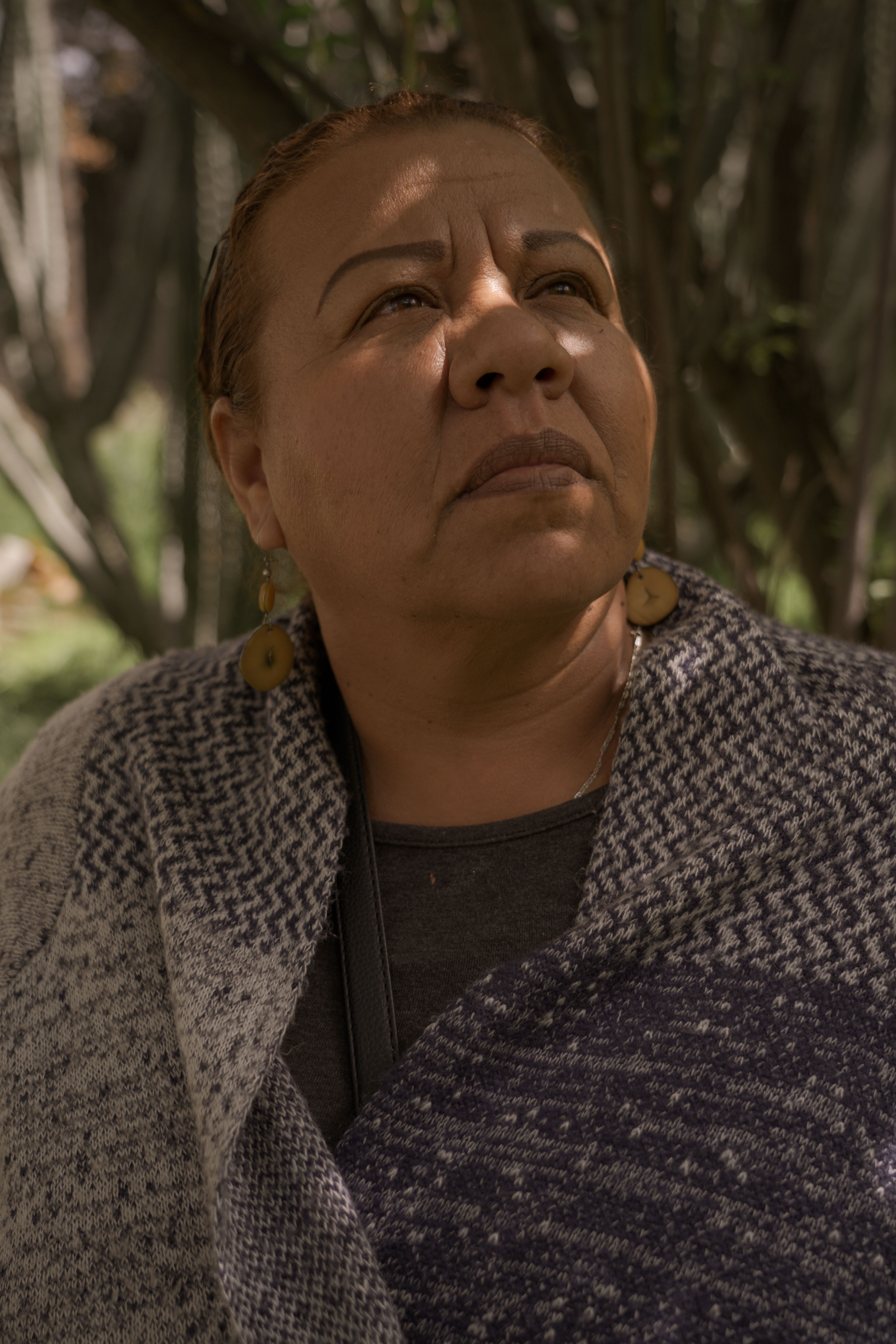 Close-up of a woman's face, looking thoughtful, wearing a grey patterned jacket.