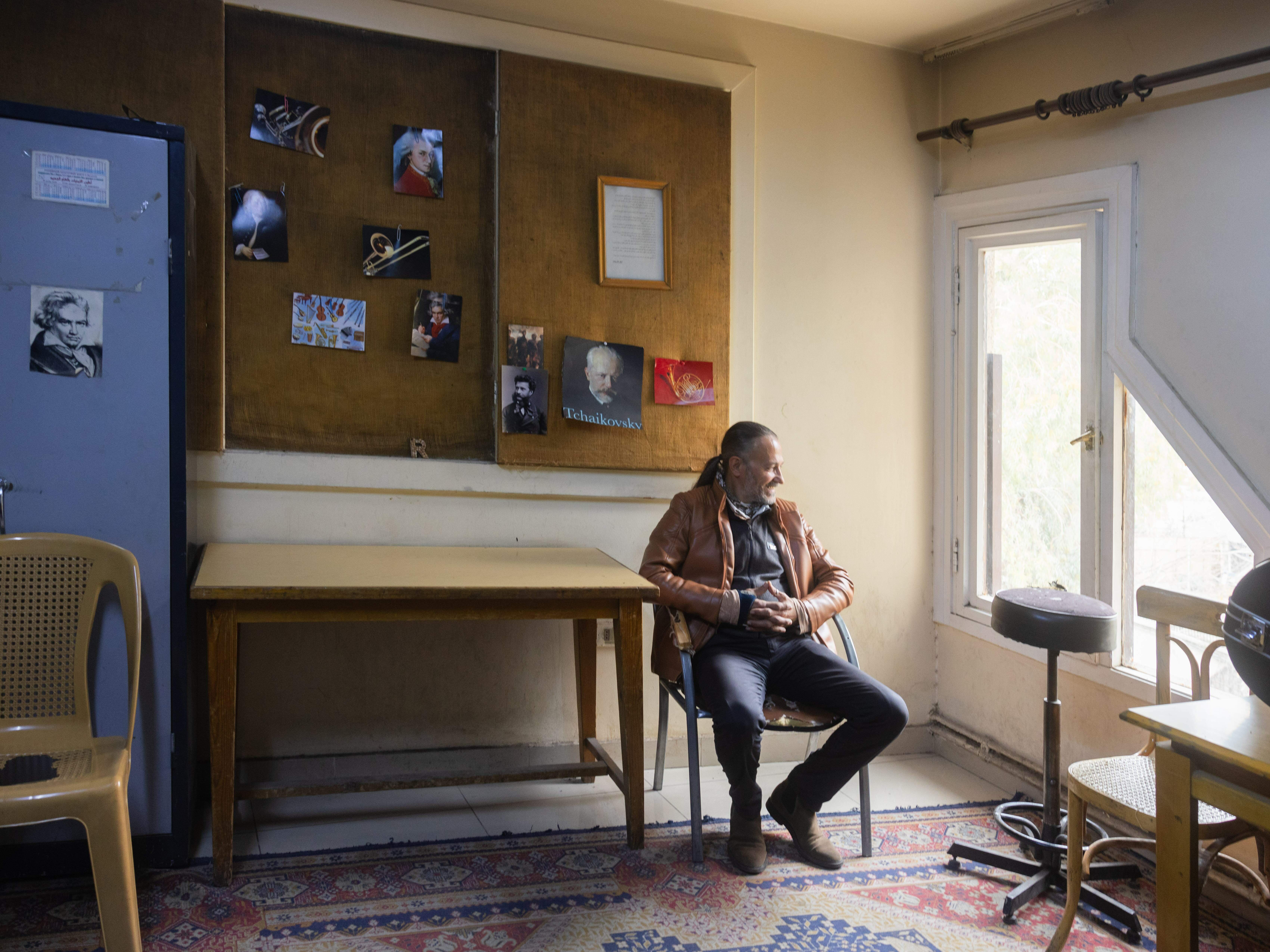 A male individual sitting at a desk in a cluttered room, with various items and artwork displayed on the walls.