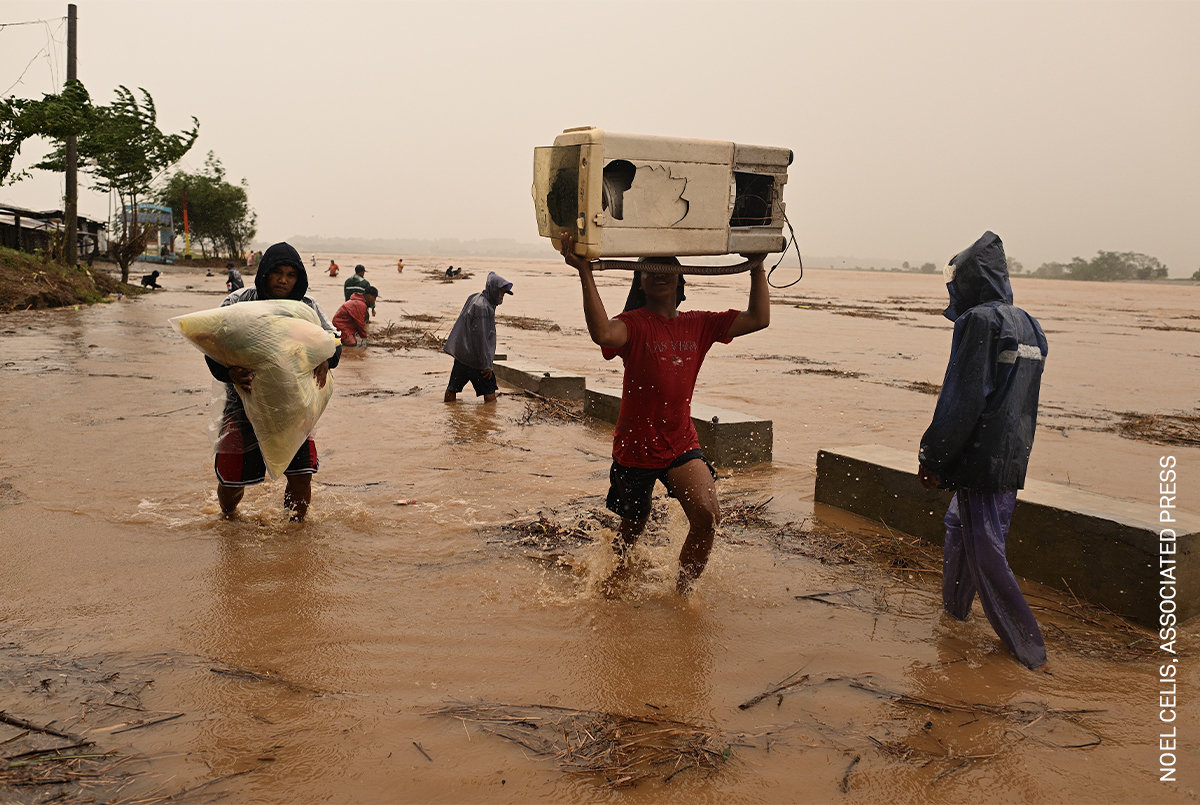 People wading through flood waters, carrying belongings on their heads.