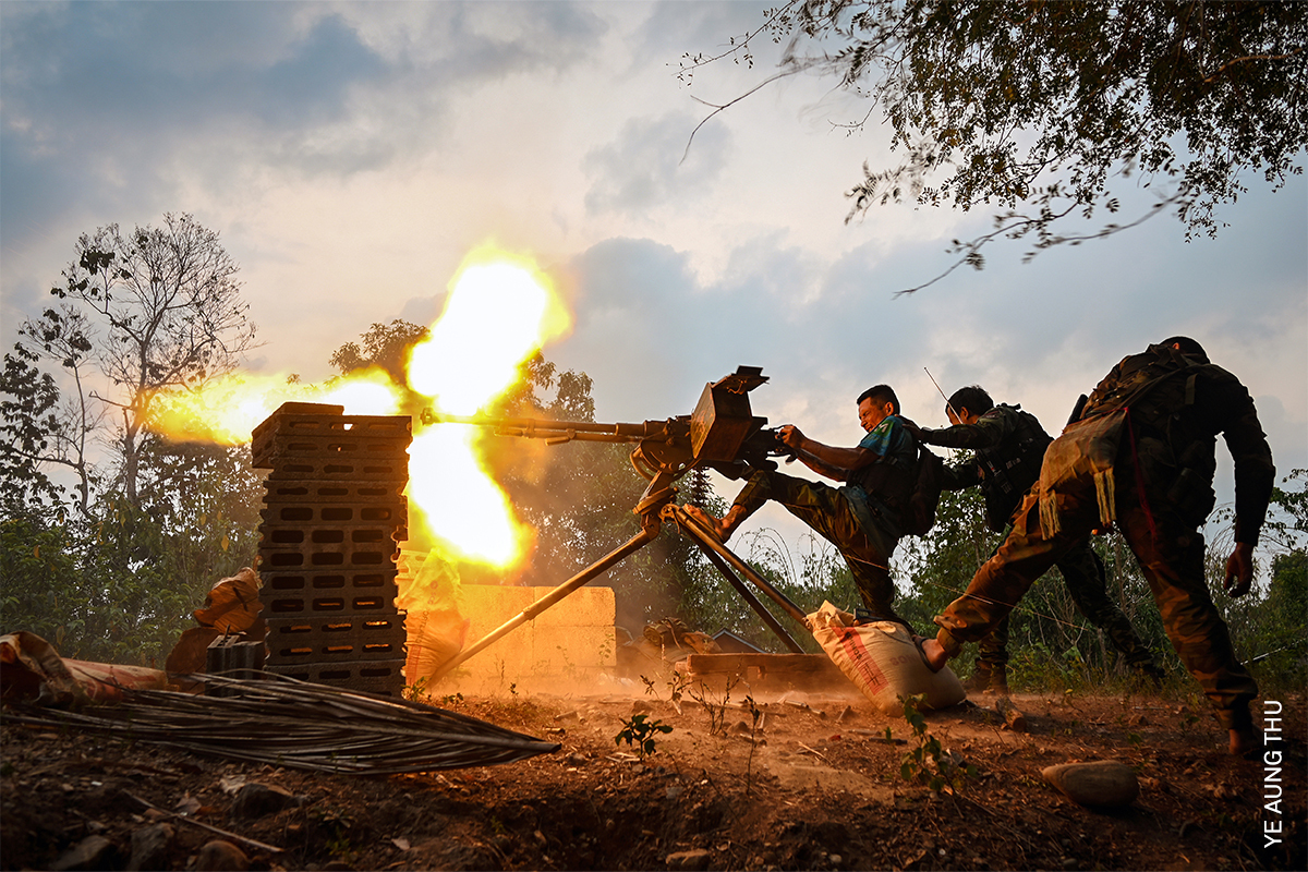 Soldiers using heavy weaponry during combat at dusk, with light and smoke visible.