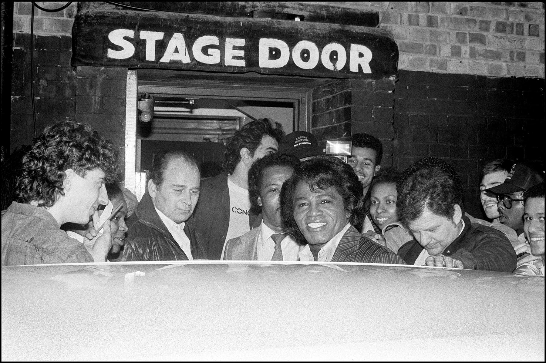 Crowd of people gathered around stage door, smiling and laughing.