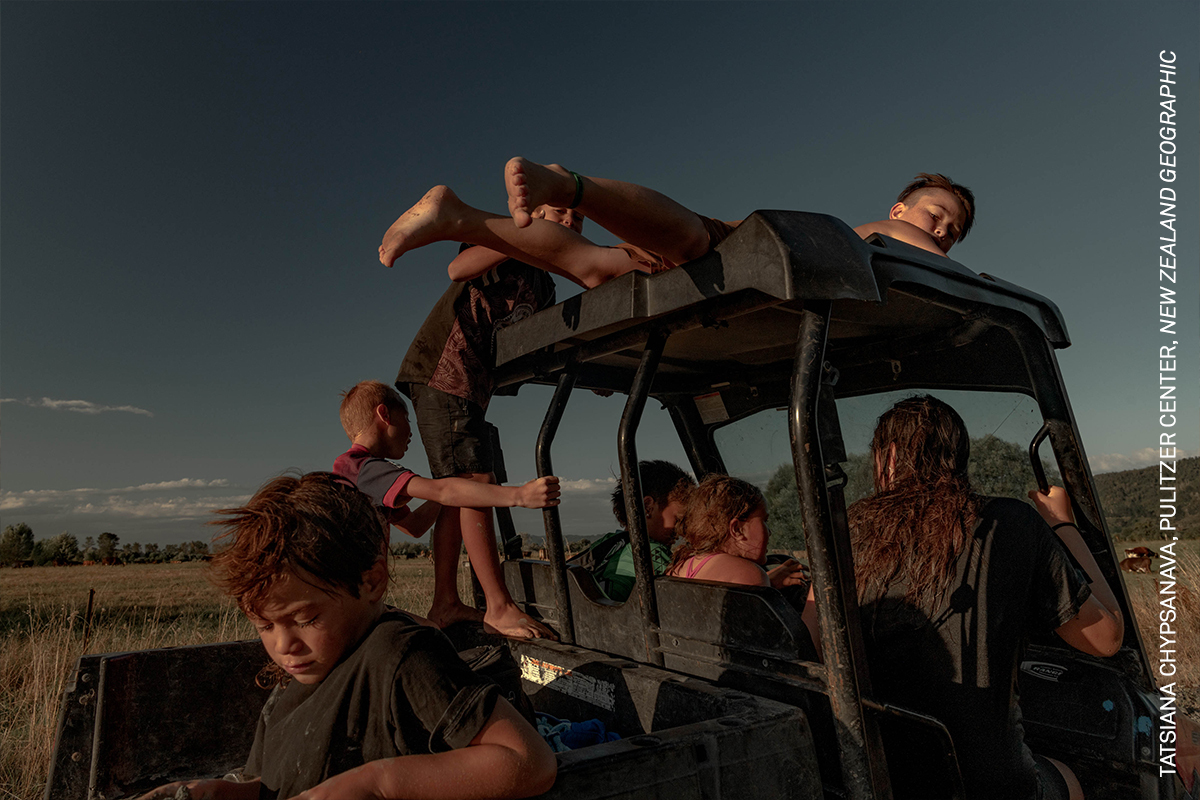 A group of people sitting in the back of a vehicle, outdoors against a cloudy sky.