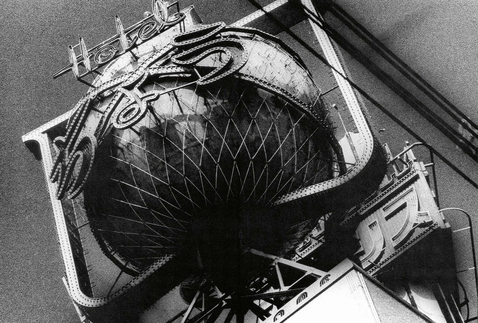 Black and white aerial view of large parabolic satellite dish with geometric grid pattern and supporting metal framework structures.