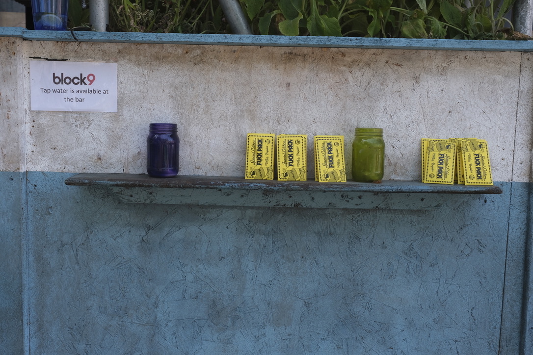 Concrete shelving with Block9 sign, displaying yellow packets, dark jar, and green container against blue-painted wall.