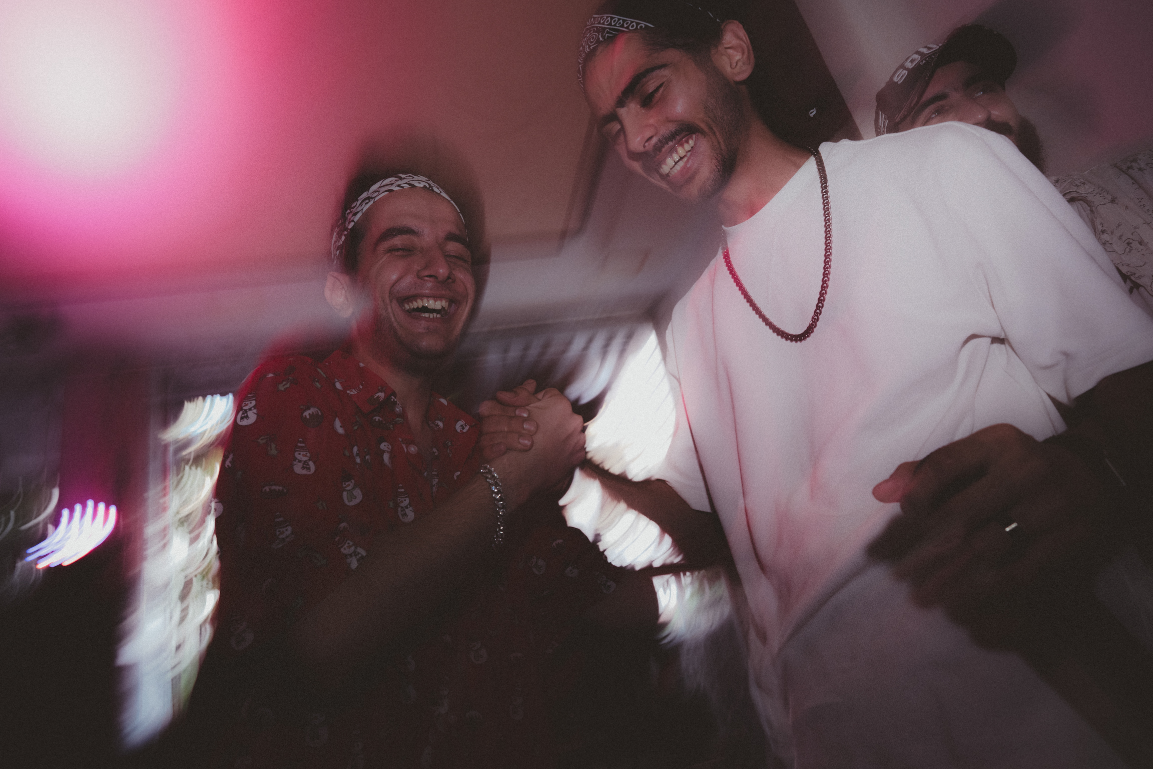 Two smiling men embracing indoors with pink lighting and motion blur effects