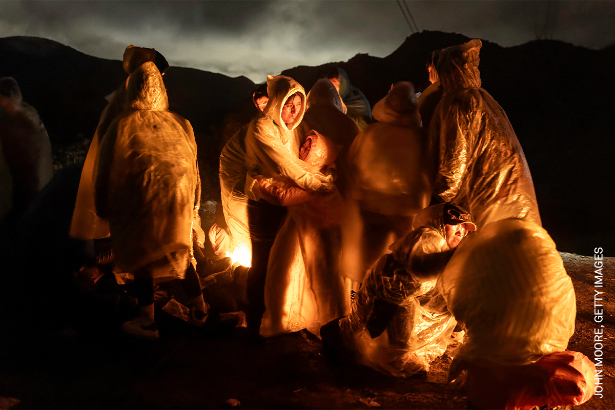 Warm-toned figures gathered around a campfire, shrouded in shadowy light and dark hues.