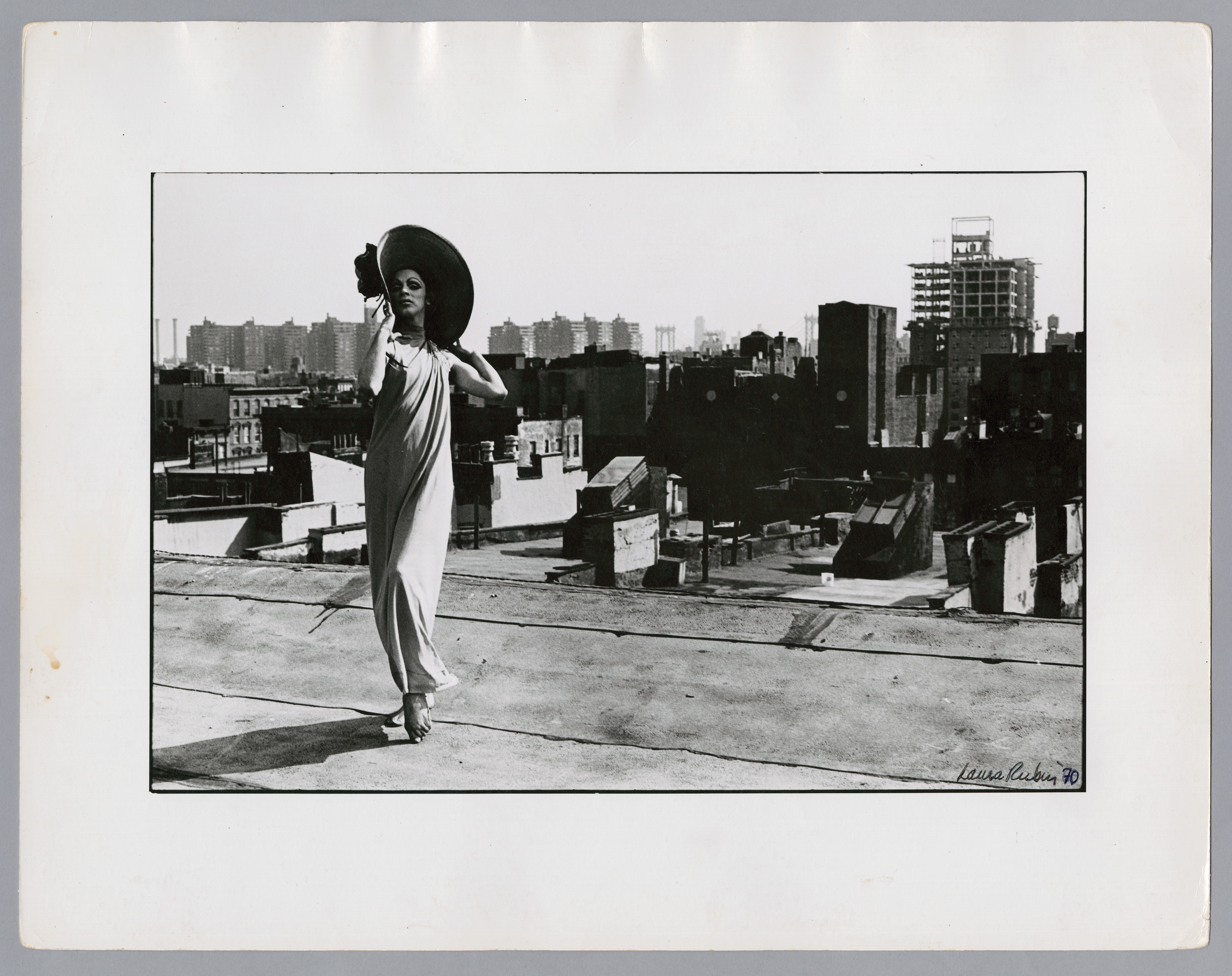 Black and white image of a person in a flowing dress walking through an urban landscape with skyscrapers and other buildings in the background.