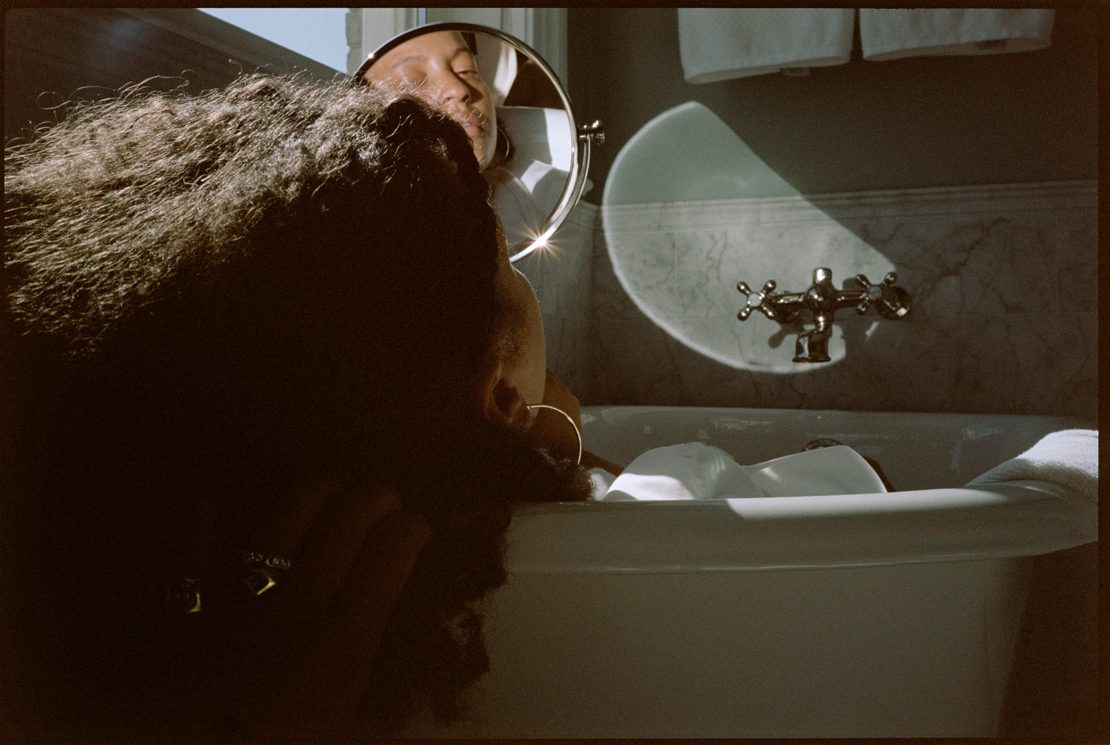 Person in brown fur coat looking through circular window showing spacecraft in distance against pale green sky.