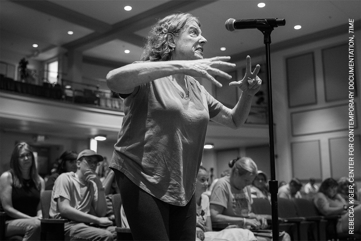 Monochrome image of a person performing on a stage, gesturing animatedly.