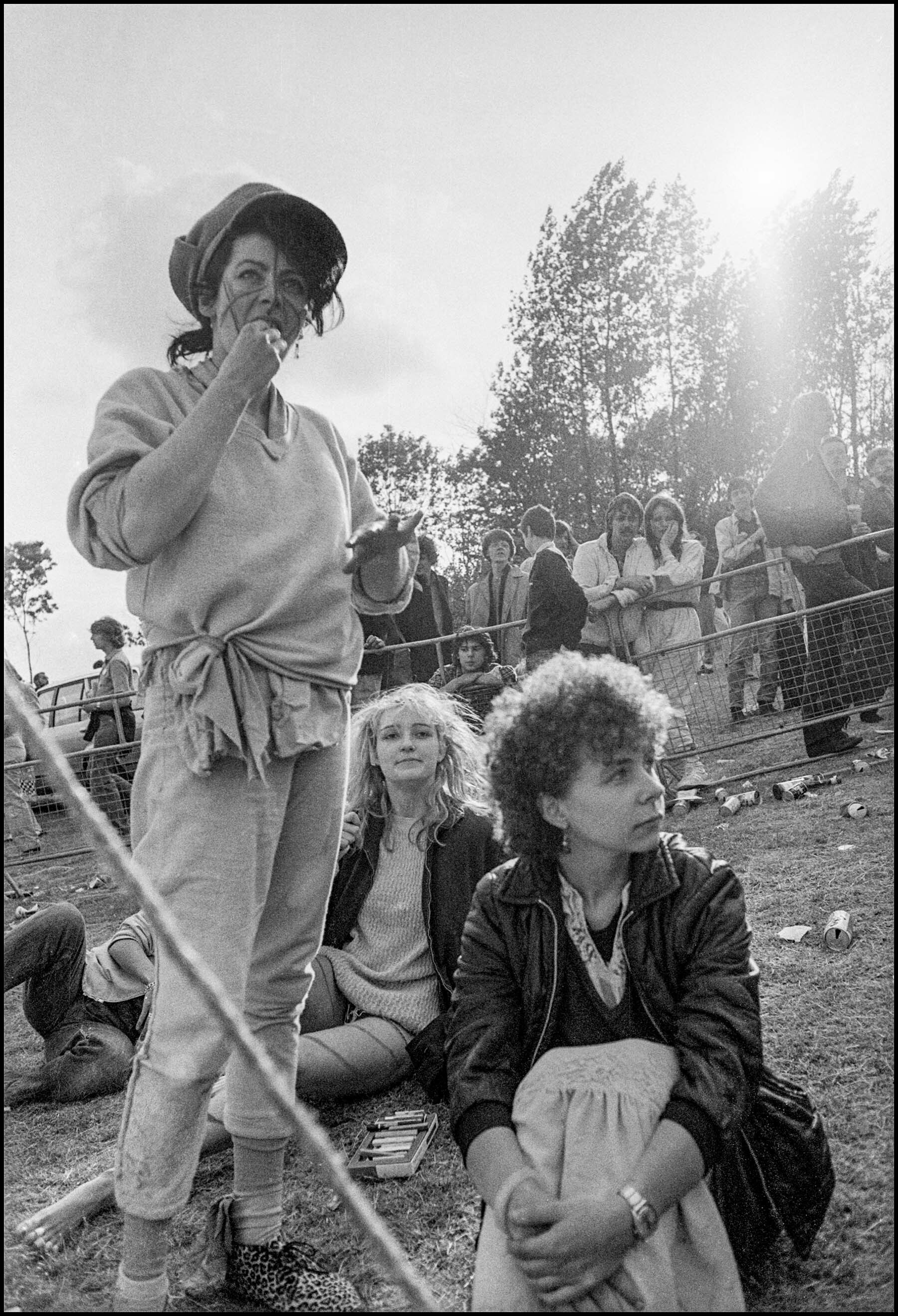 Black and white image showing a group of people, including a woman wearing a hat and jacket, a woman with curly hair, and a man with a serious expression, at an outdoor event or gathering.