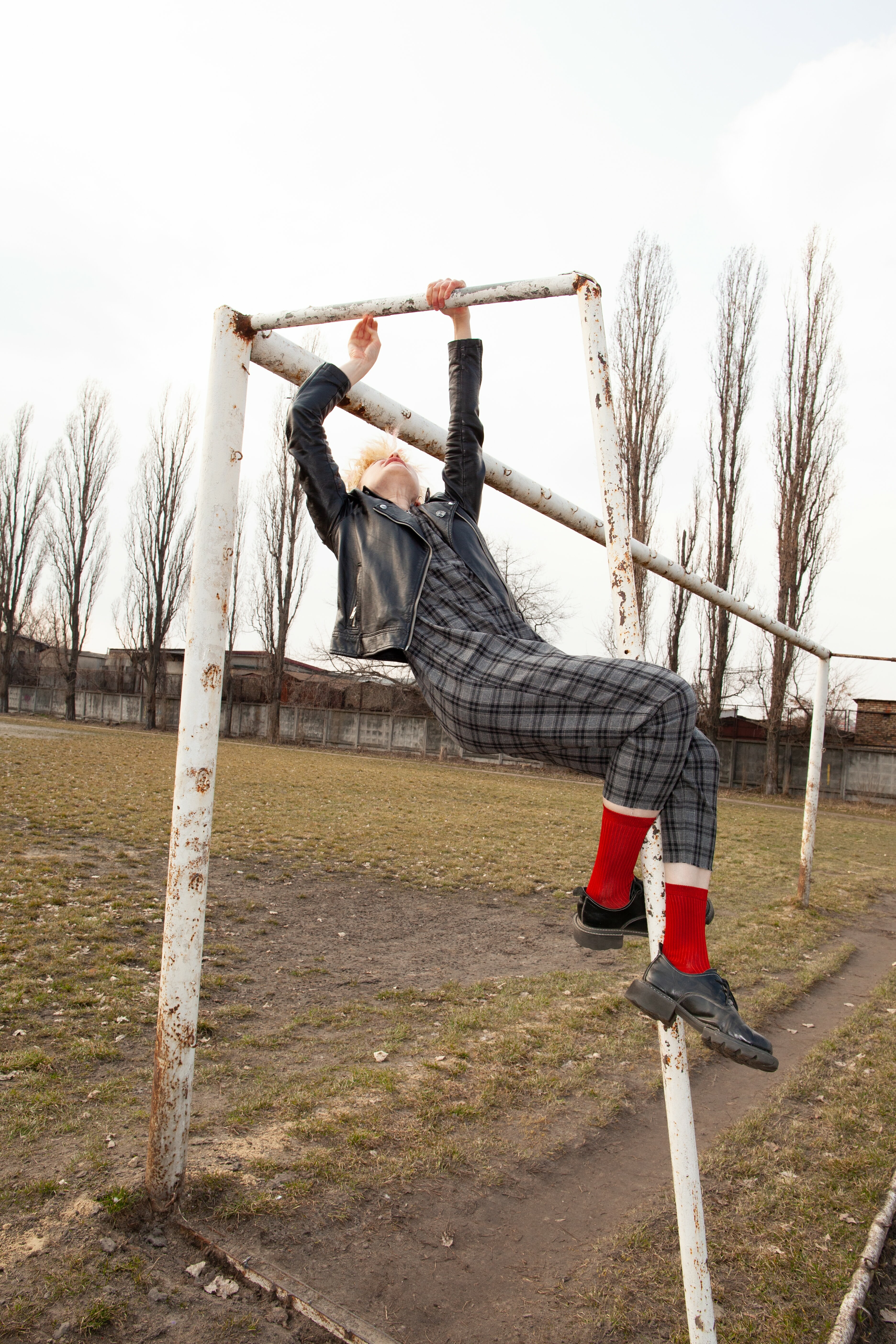 Person sitting on a frame suspended from wooden poles, wearing a checkered pattern outfit and red socks.