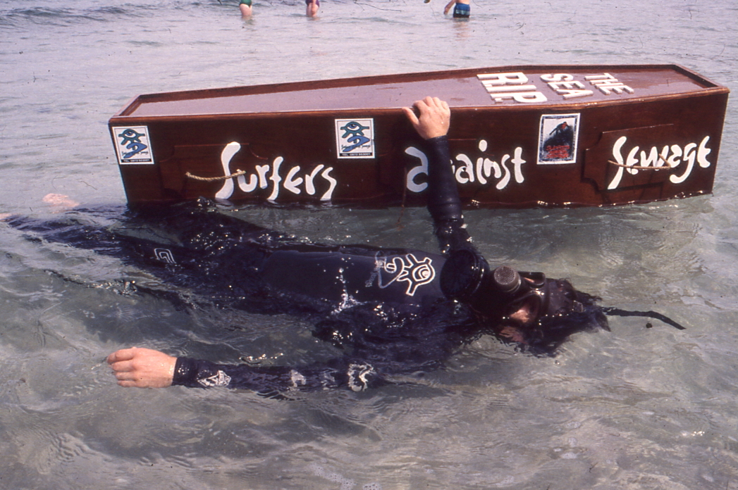 Surfers against sewage protest box floating in water with people swimming around it.