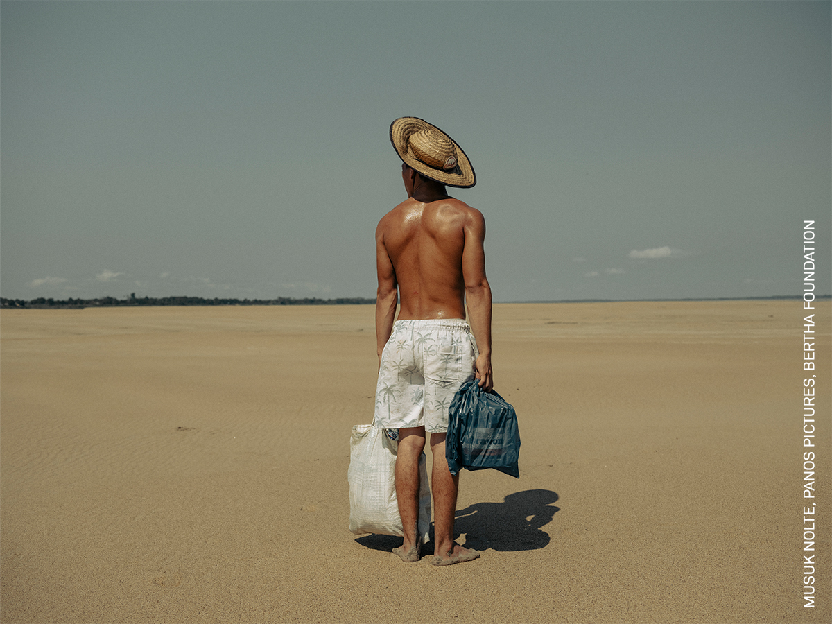 A person wearing a hat and carrying a bag, standing alone on a sandy beach.