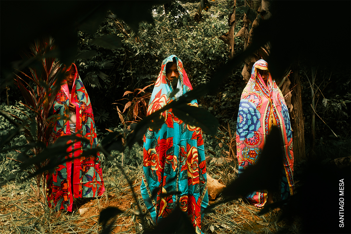 Colourful flowtuing fabrics worn by three people, walking through a lush green forest.