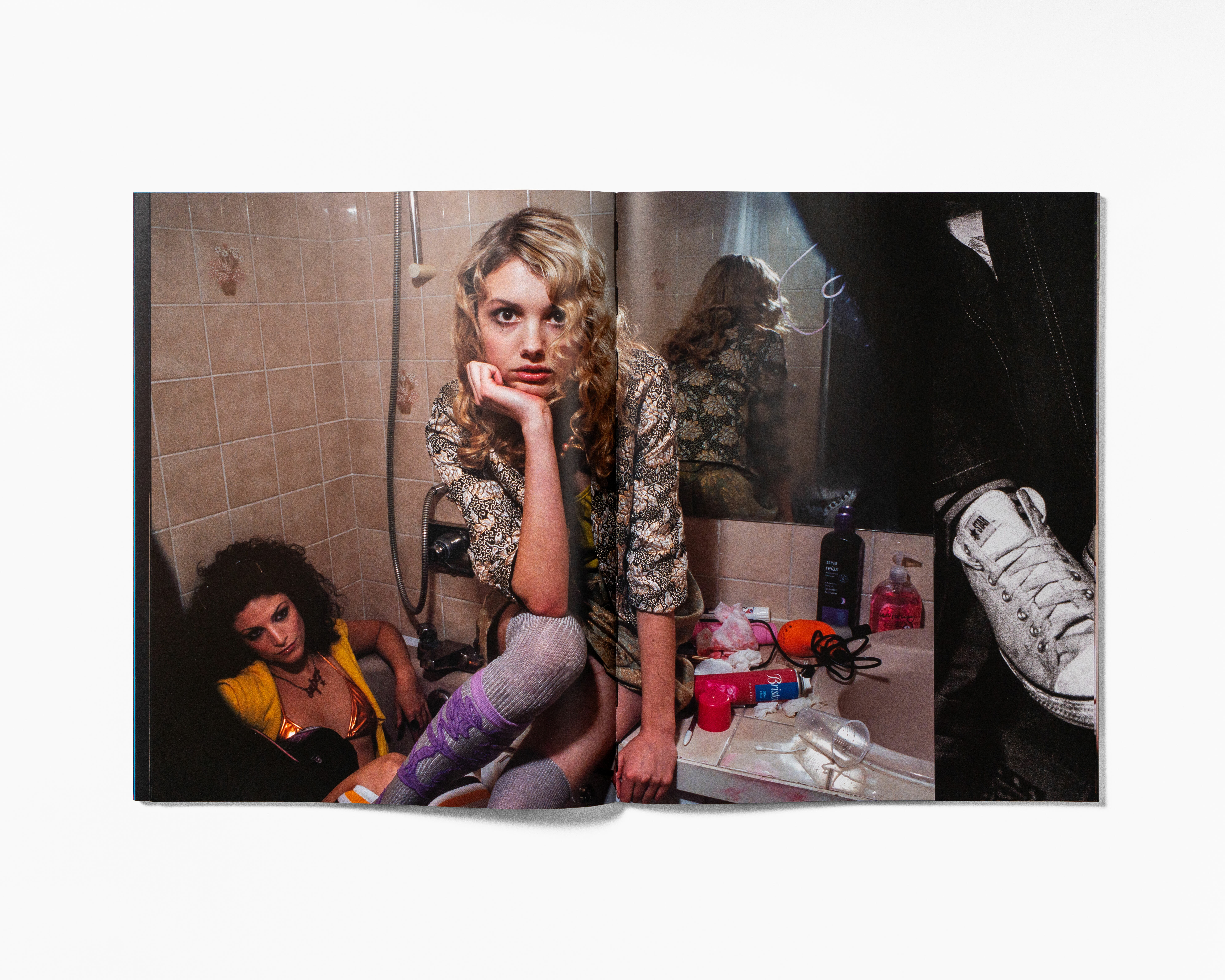 Two people in a messy room, one sitting on the floor, the other leaning against a wall.