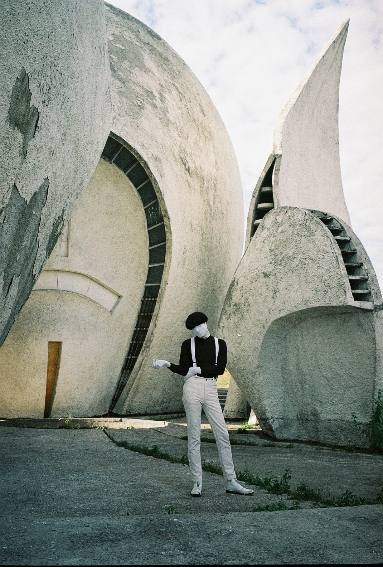 Curving grey concrete structures with angled roofs and windows, person in casual clothing standing in foreground.