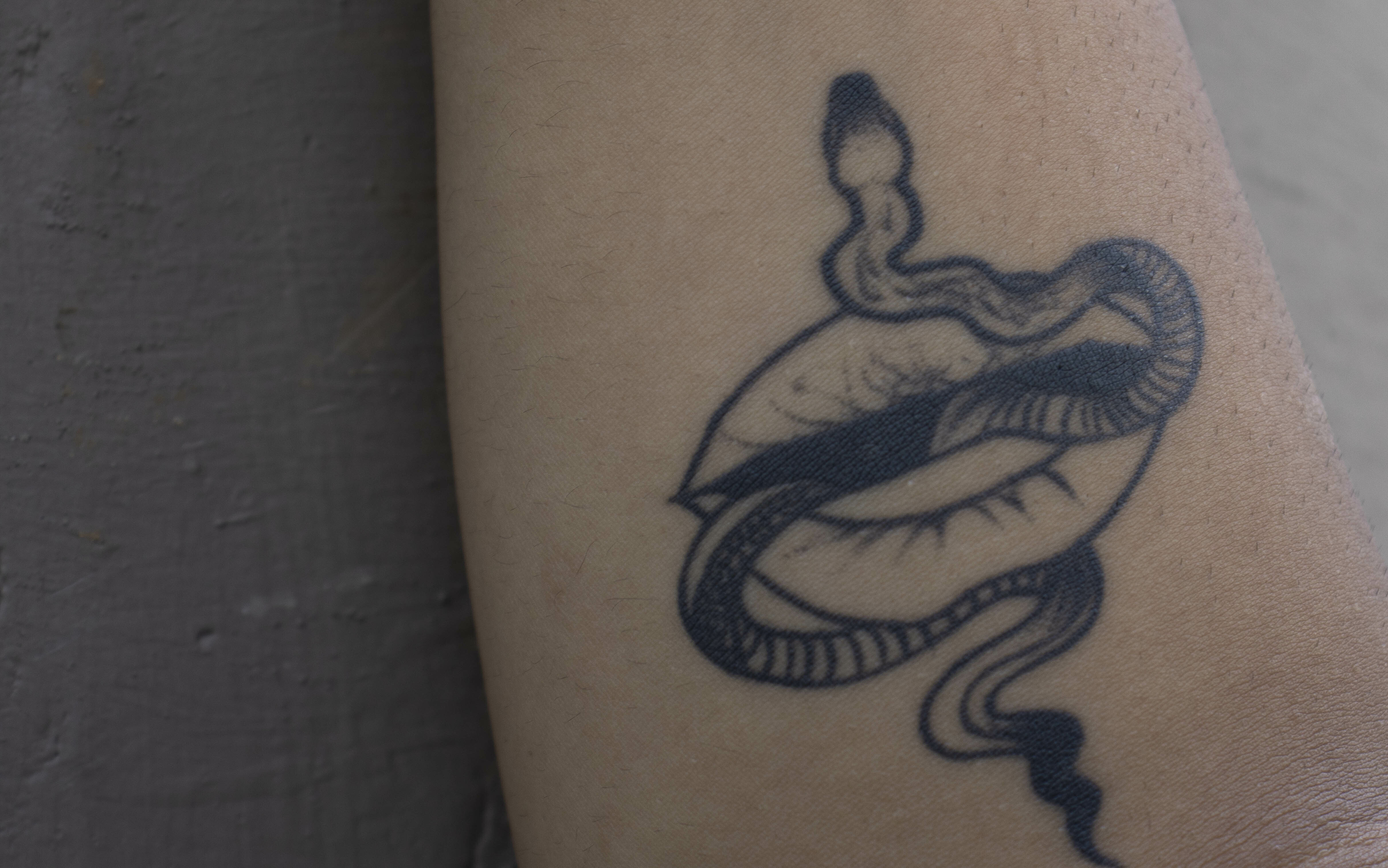 Intricate tattoo of an abstract, serpentine creature with flowing, sinuous lines and a stylised eye shape.